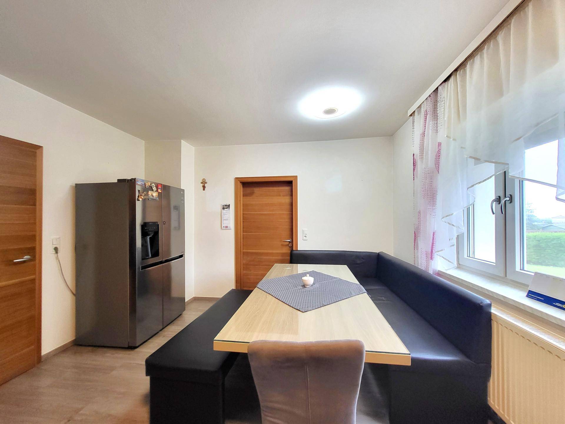 Gemütlicher Essbereich mit Eckbank und großem Kühlschrank neben einem Fenster.