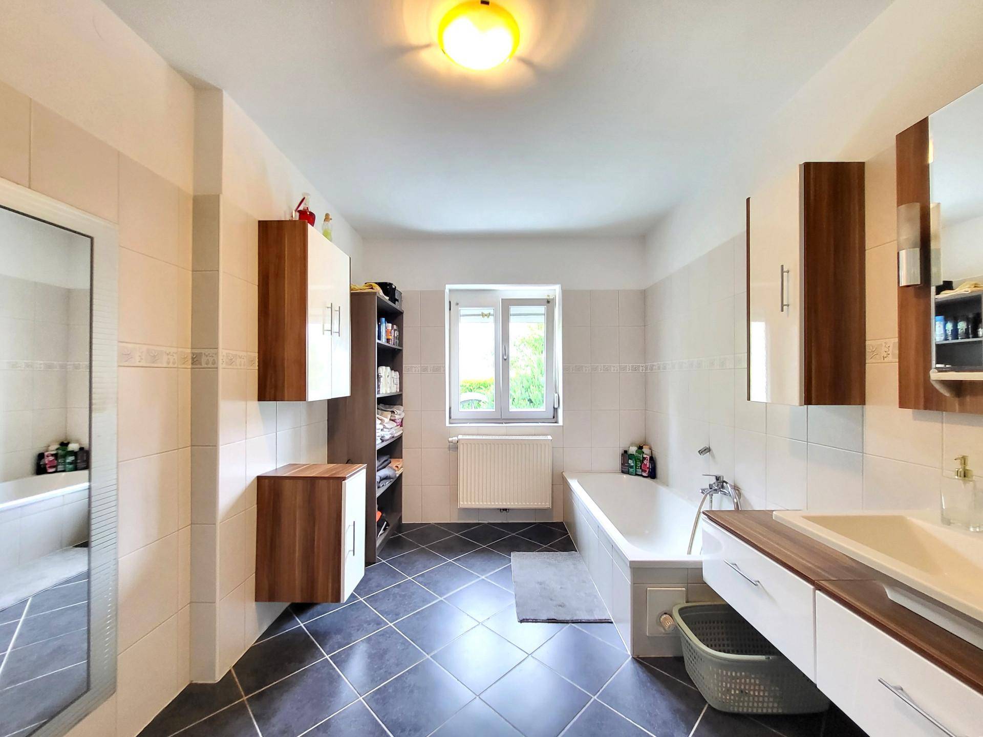 Geräumiges Badezimmer mit Badewanne, Fliesenboden und Fenster für Tageslicht.