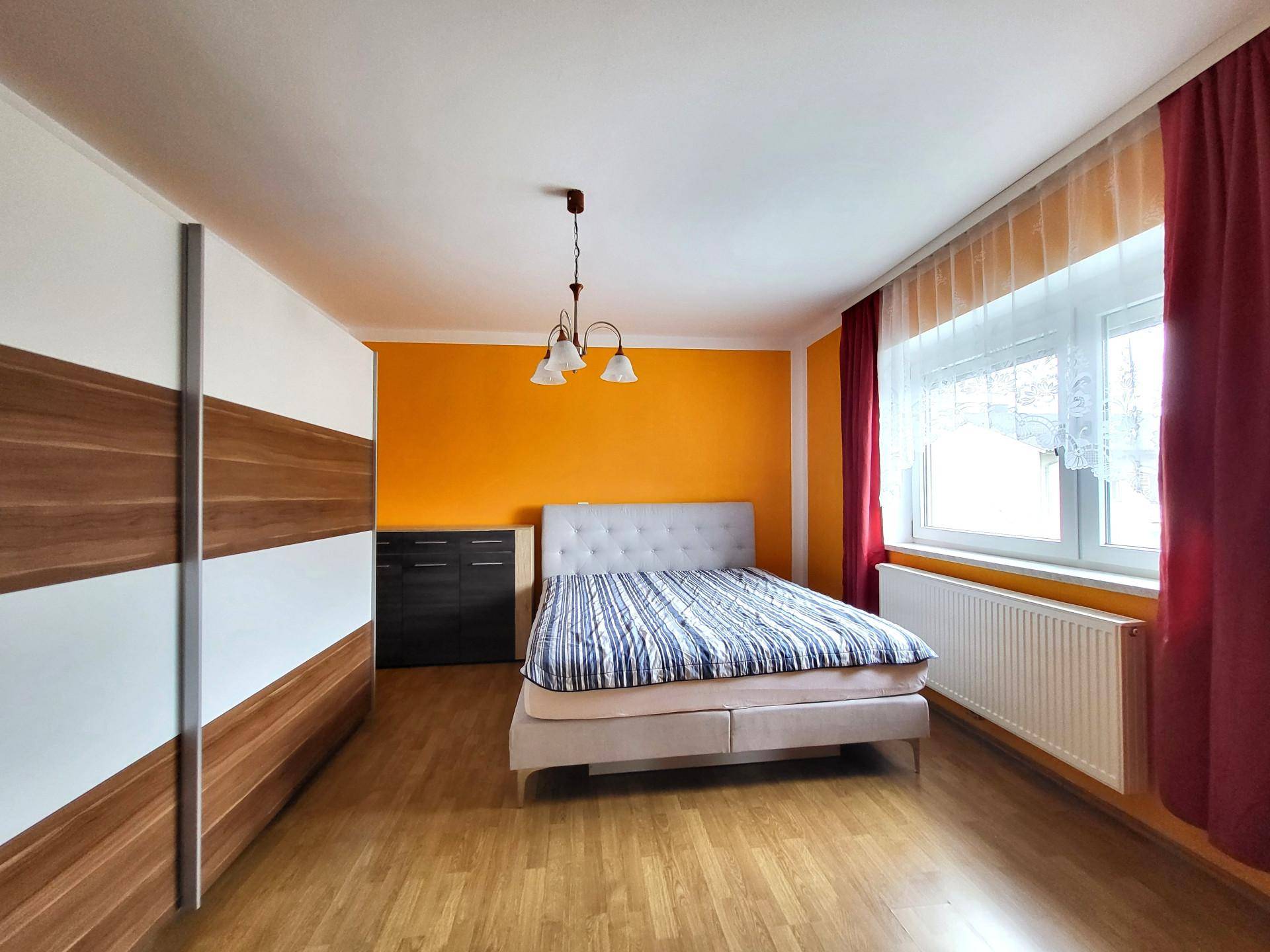Schlafzimmer mit orangefarbener Akzentwand, Doppelbett und Holzschrank.