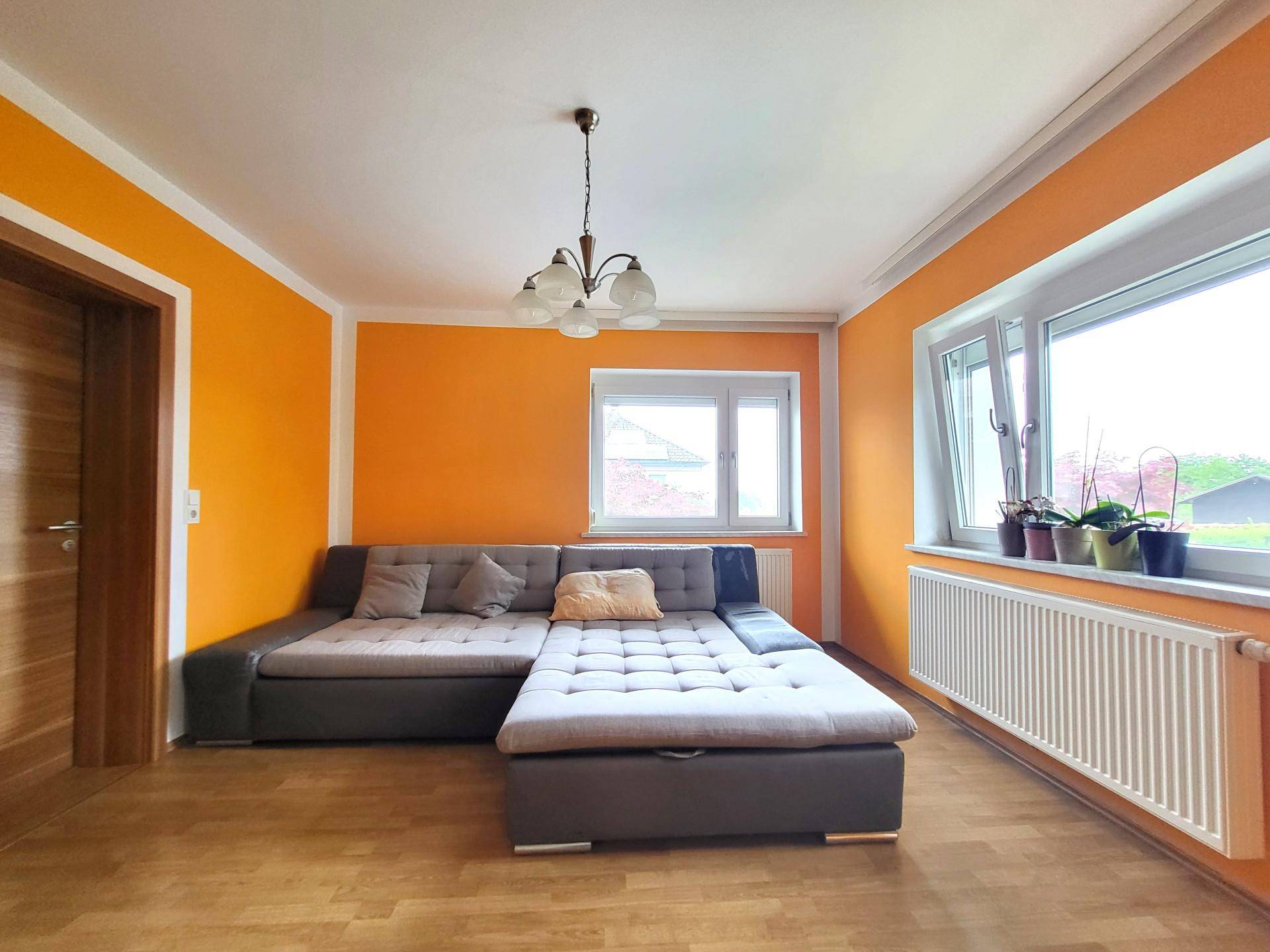 Helles Wohnzimmer mit orangefarbenen Wänden, großem Ecksofa und Holzboden.