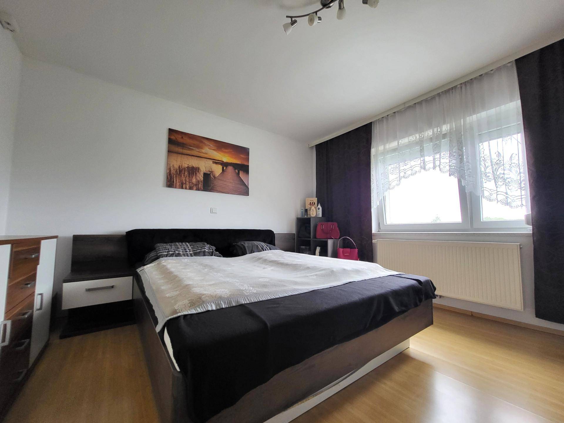 Schlafzimmer mit Doppelbett, Holzboden und großem Fenster mit dunklen Vorhängen.