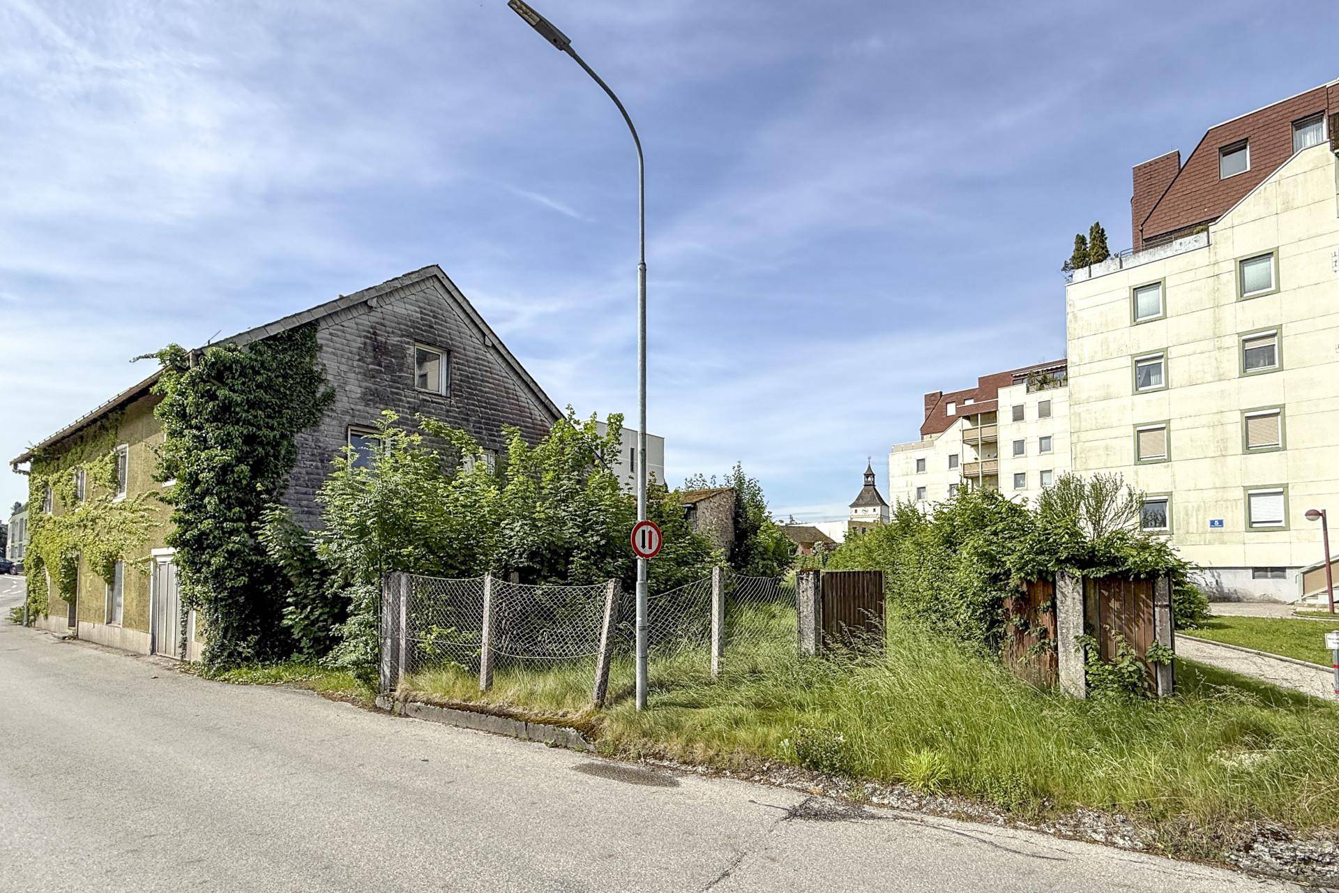 Altes, von Efeu bewachsenes Haus neben einem verwilderten Grundstück mit Zaun und Straßenlaterne.