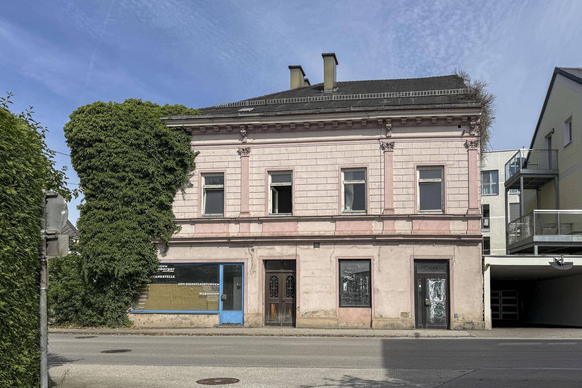 Historisches Gebäude mit rosa Fassade, Stuckelementen und Ladenflächen im Erdgeschoss an einer Straße.