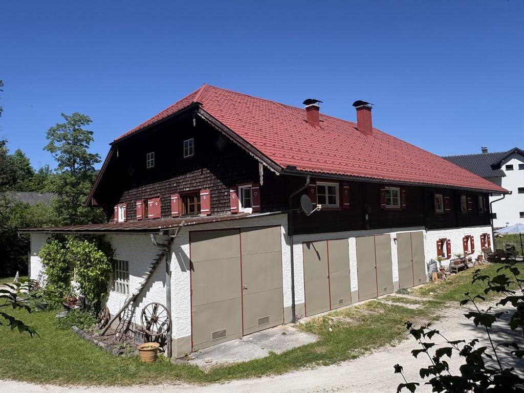 Traditionelles Bauernhaus mit Garagen im Erdgeschoss und rotem Dach.