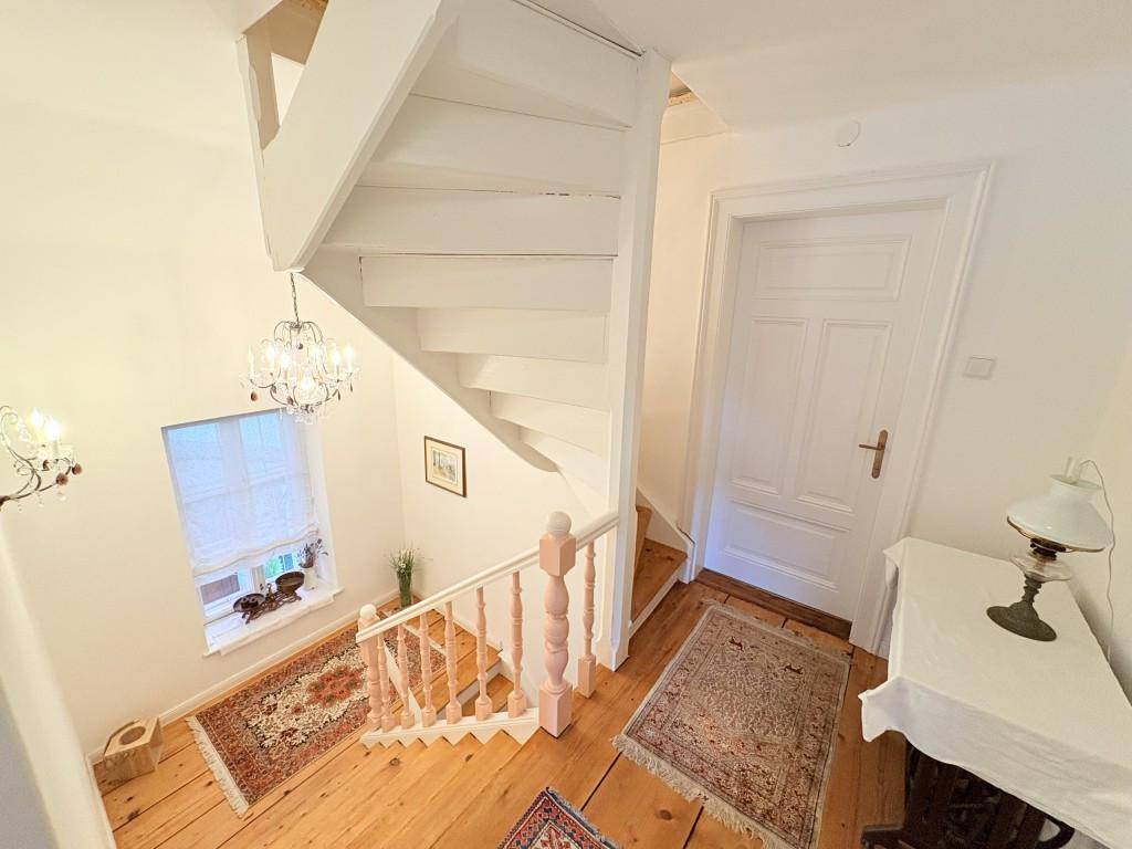 Helles Treppenhaus mit Holztreppe und Holzboden, geschmückt mit traditionellen Teppichen.