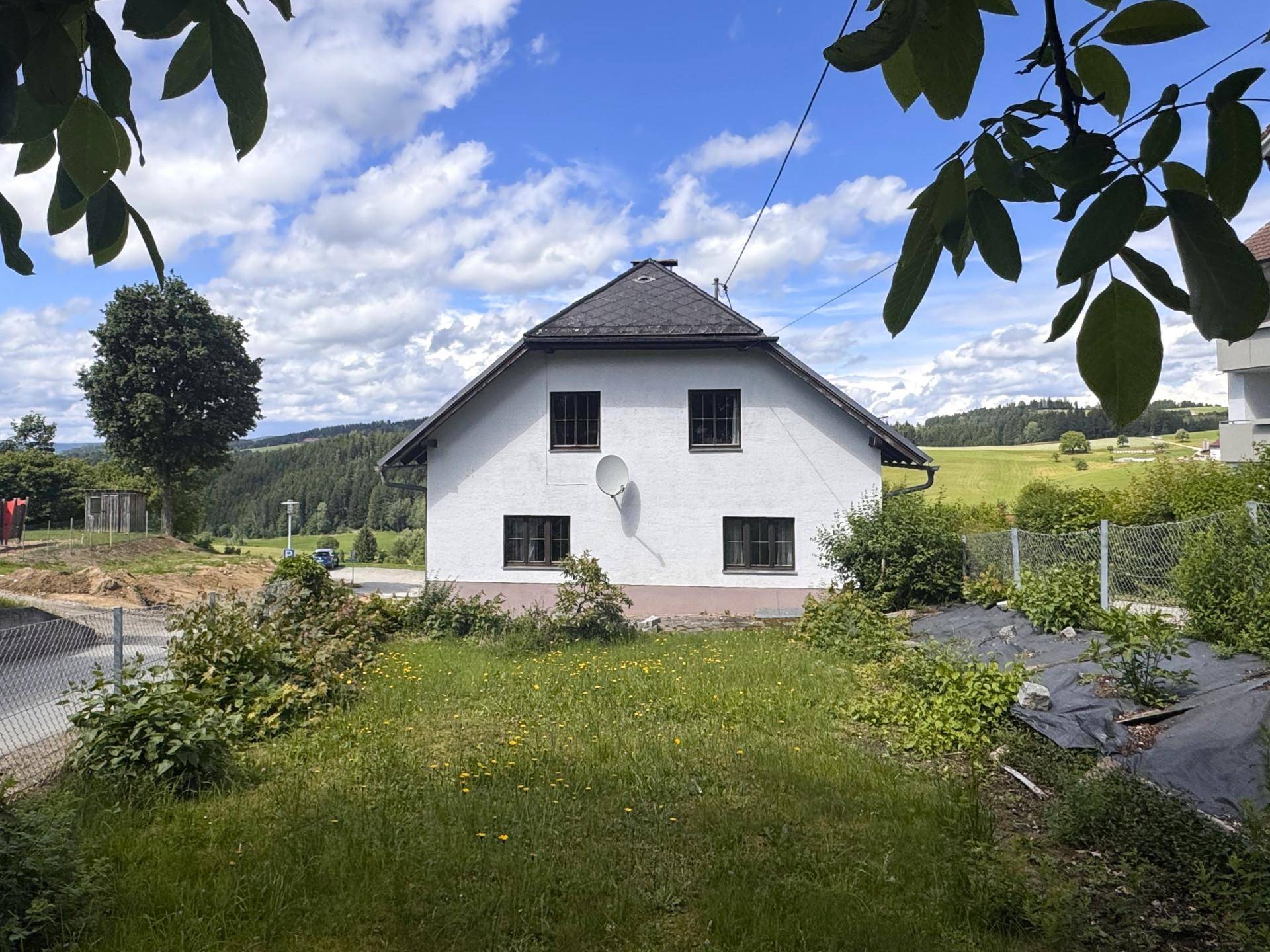 Rückseite des weißen Hauses mit Gartenbereich und weitem Blick auf die umliegende Landschaft.
