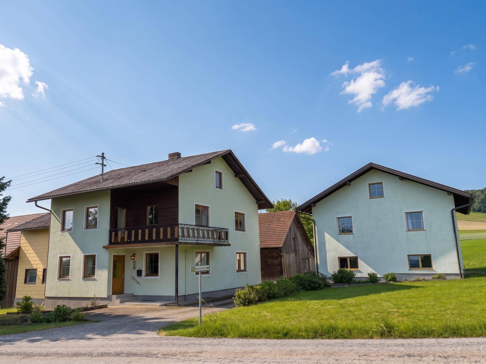 Hauptgebäude mit hellgrüner Fassade, Holzbalkon und Satteldach in ländlicher Umgebung.