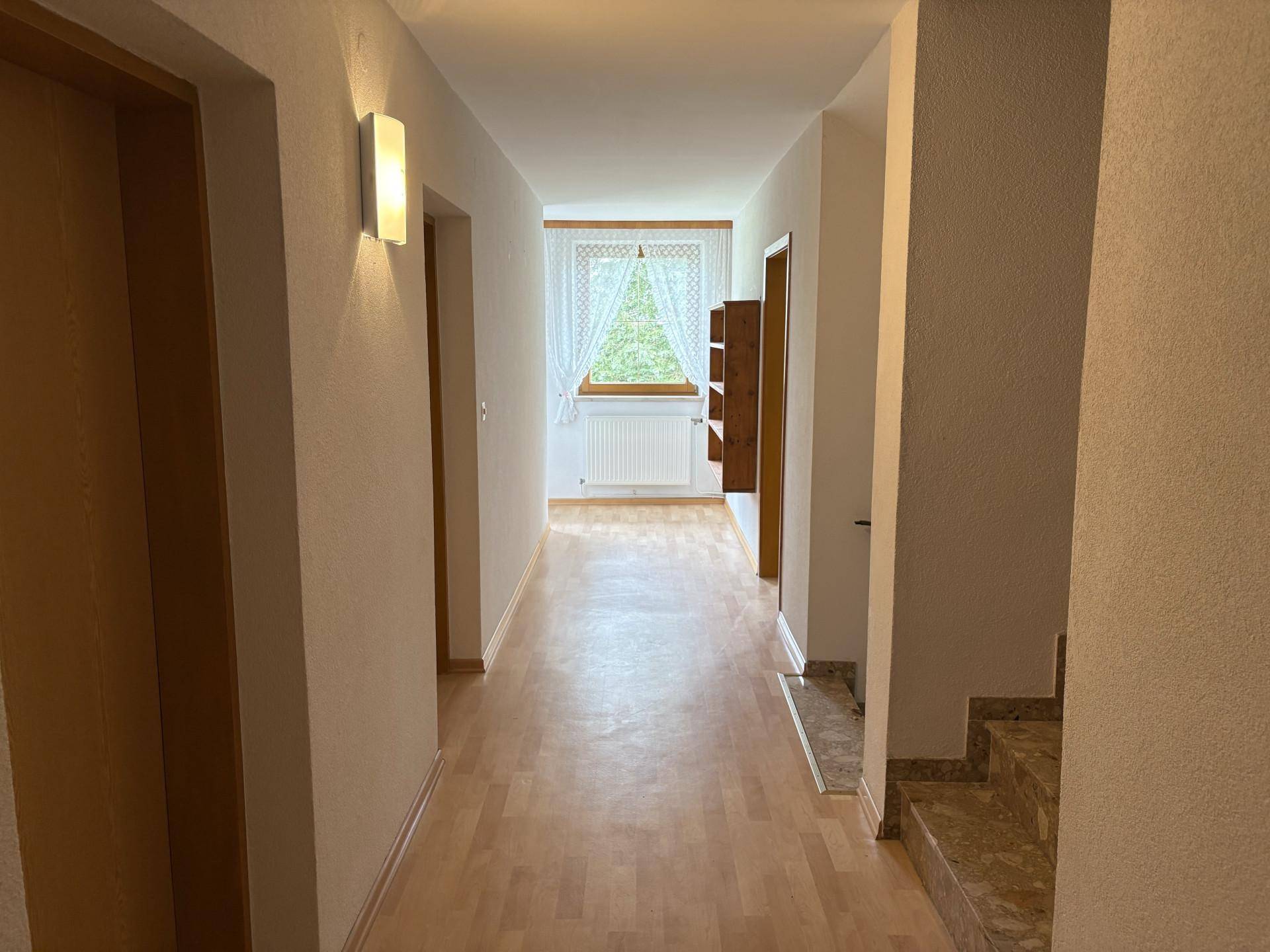 Heller Flur mit Laminatboden, weiß gestrichenen Wänden und einem Fenster am Ende.