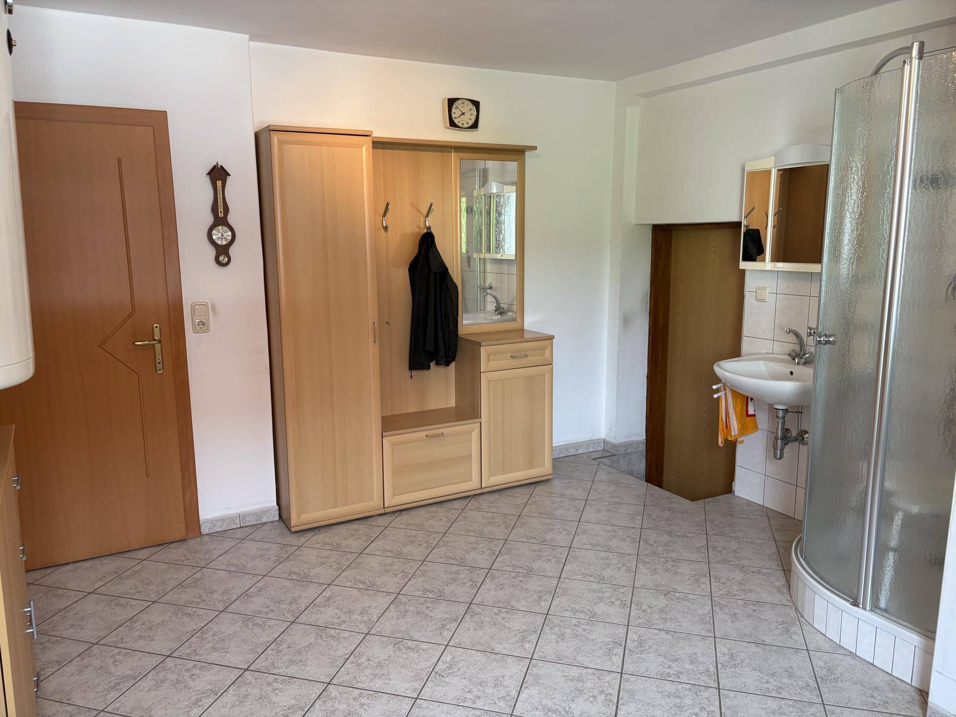 Einfaches Badezimmer mit Duschkabine, Waschbecken und Fliesenboden, kombiniert mit einem Garderobenbereich.