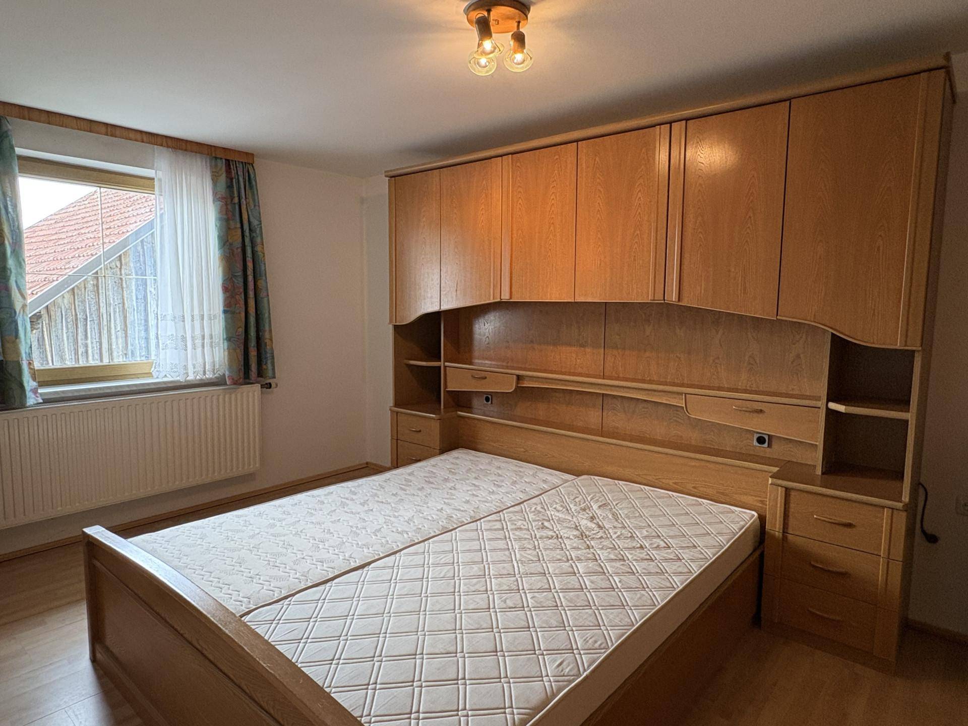 Schlafzimmer mit Doppelbett, integrierten Schränken und einem Fenster mit Blick auf das Nachbargebäude.