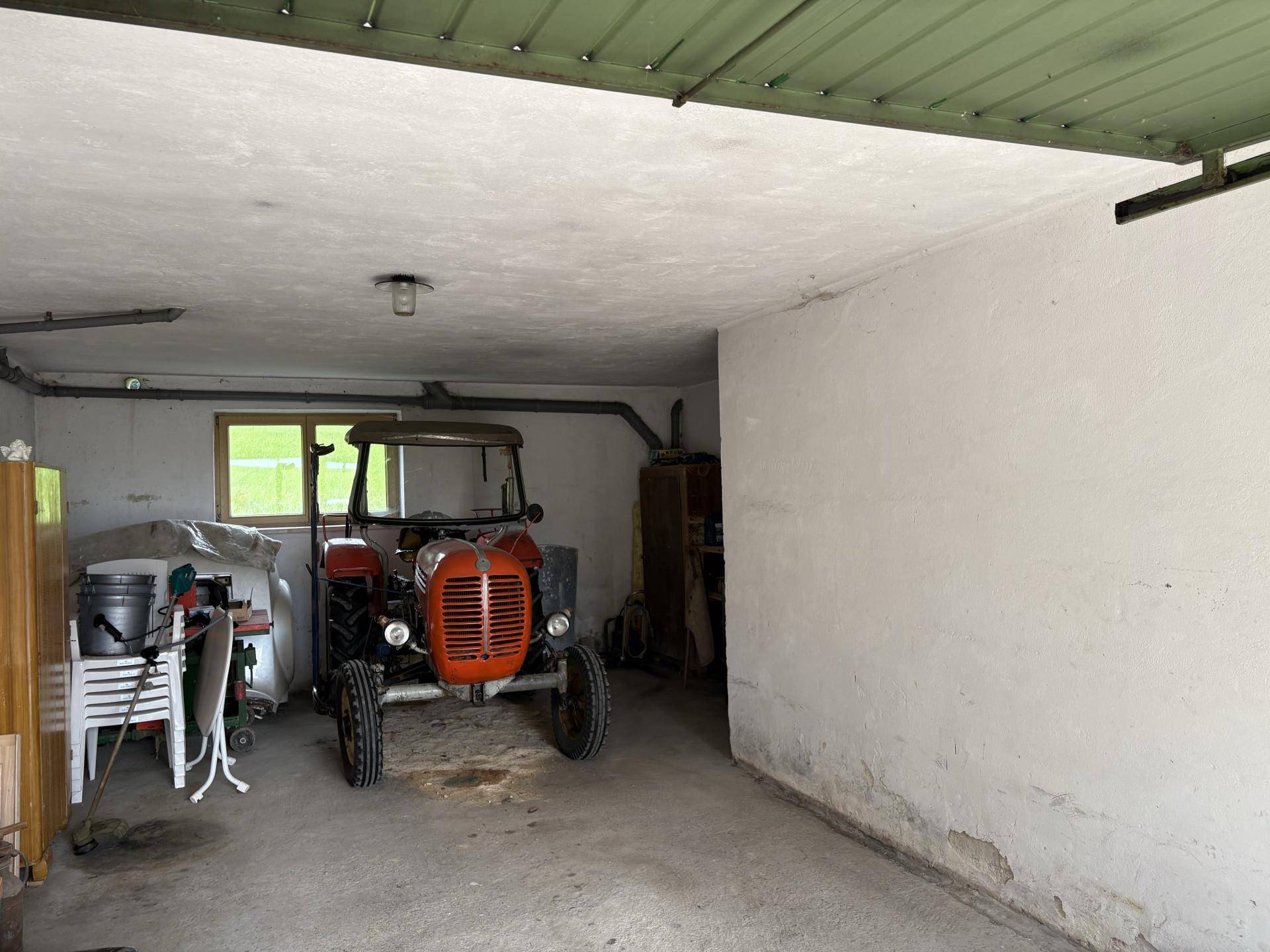 Geräumige Garage mit Betonboden, einem Fenster und einem alten Traktor.