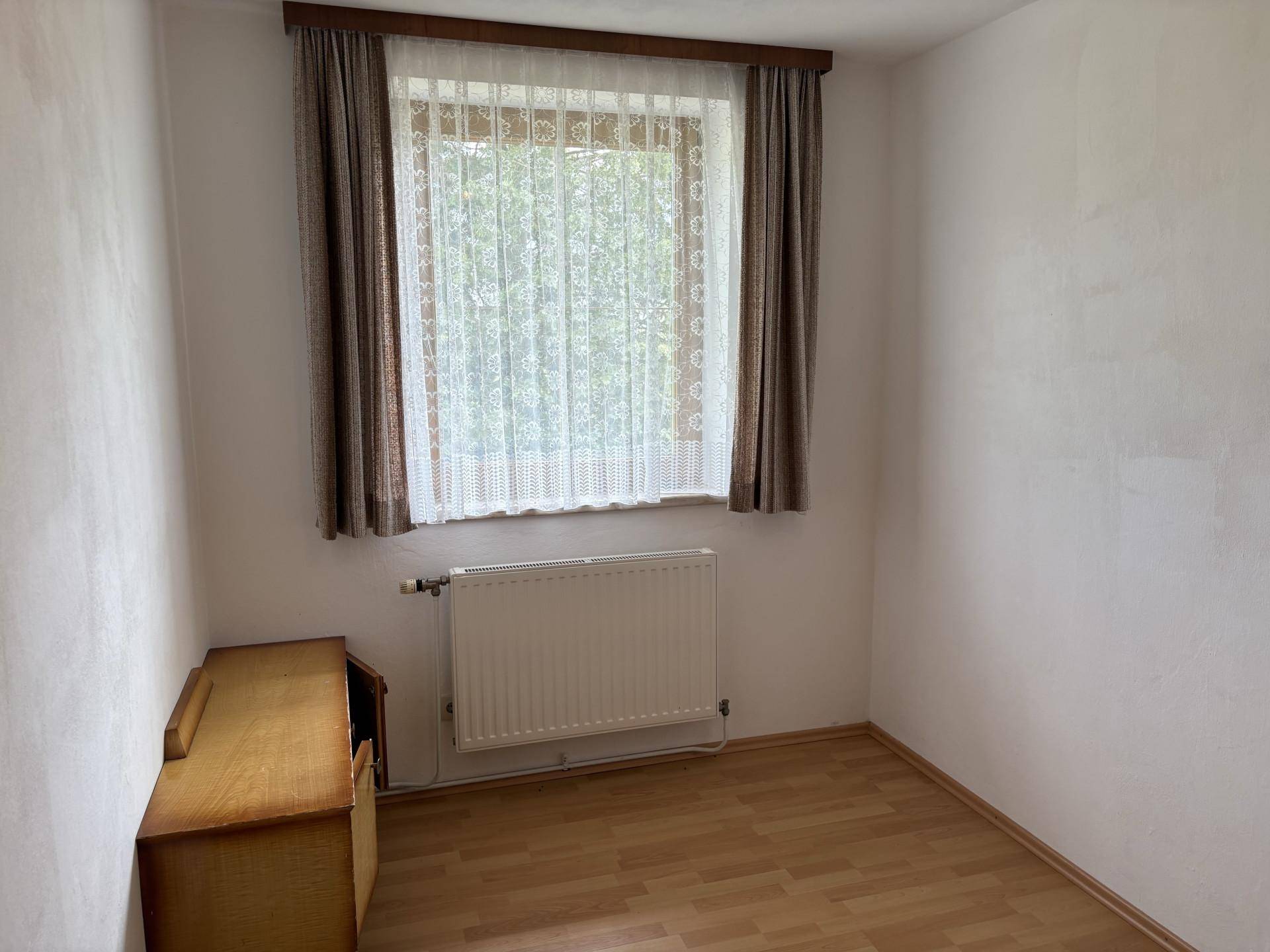 Kleines, helles Zimmer mit Laminatboden, einem Fenster und einem Heizkörper unter dem Fenster.
