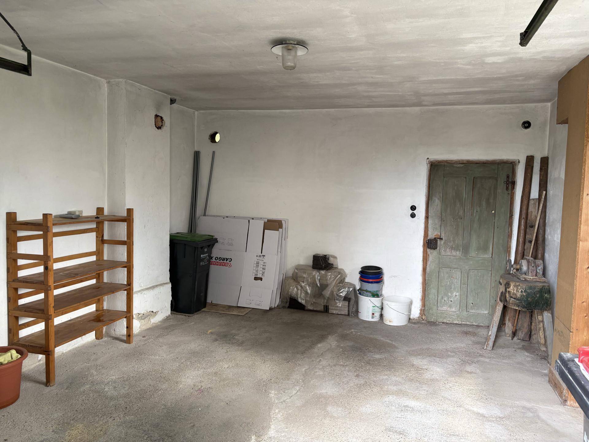Leere Garage mit Betonboden, Regalen und einer alten Holztür, ideal als Abstellraum.