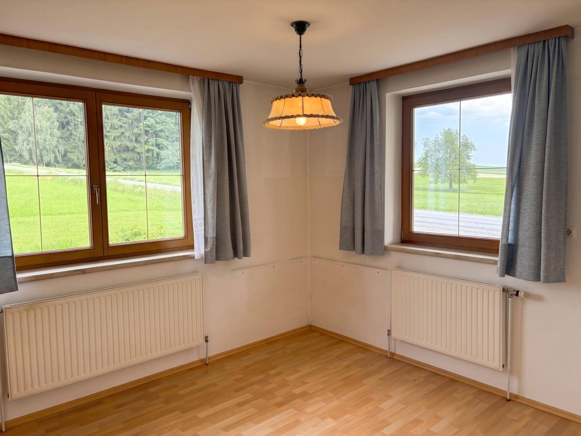 Heller Raum mit Laminatboden, zwei Fenstern mit Blick ins Grüne und einem Heizkörper.
