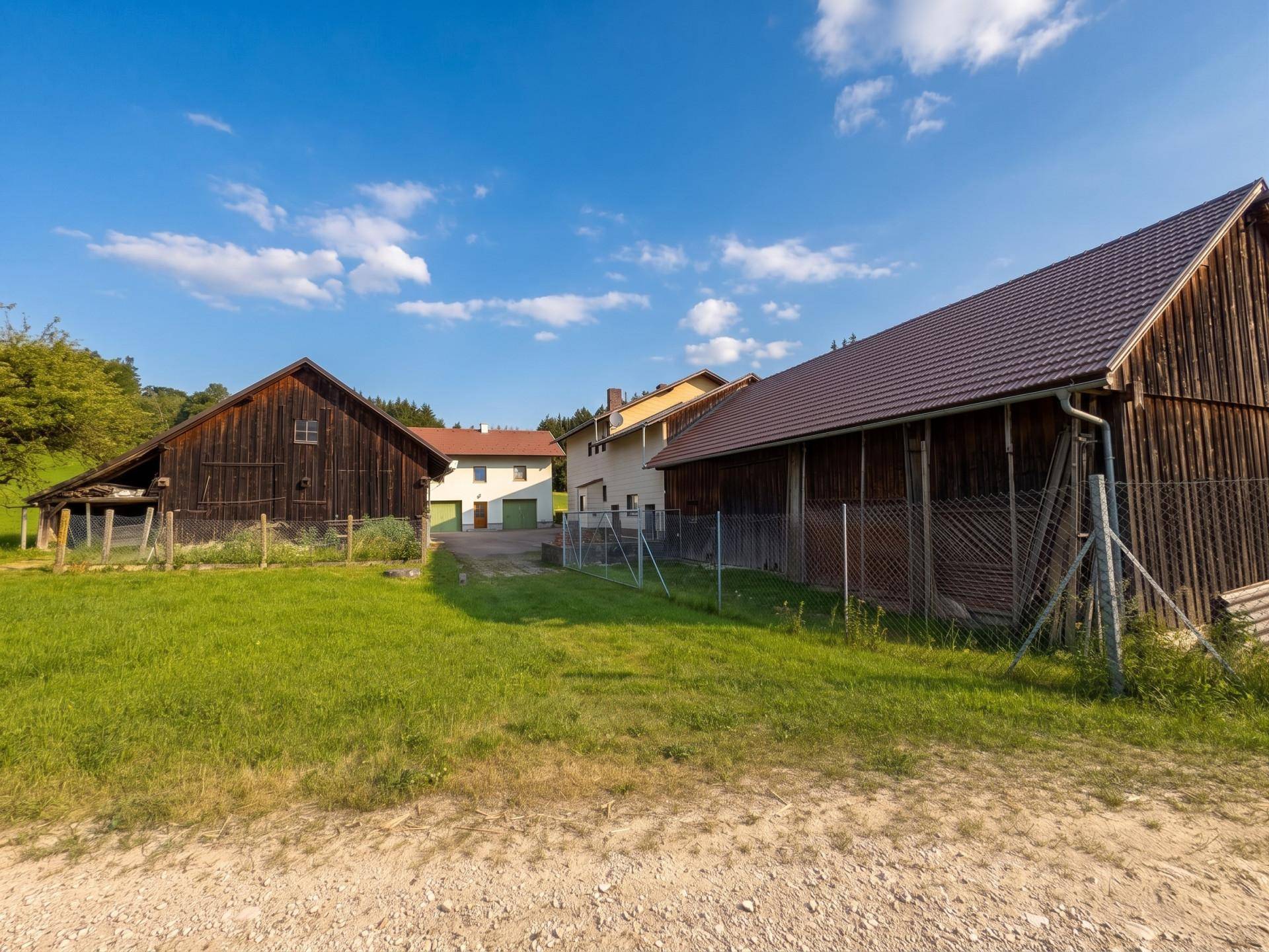 Ländliches Anwesen mit mehreren Gebäuden, darunter zwei große Holzscheunen und ein Wohnhaus.