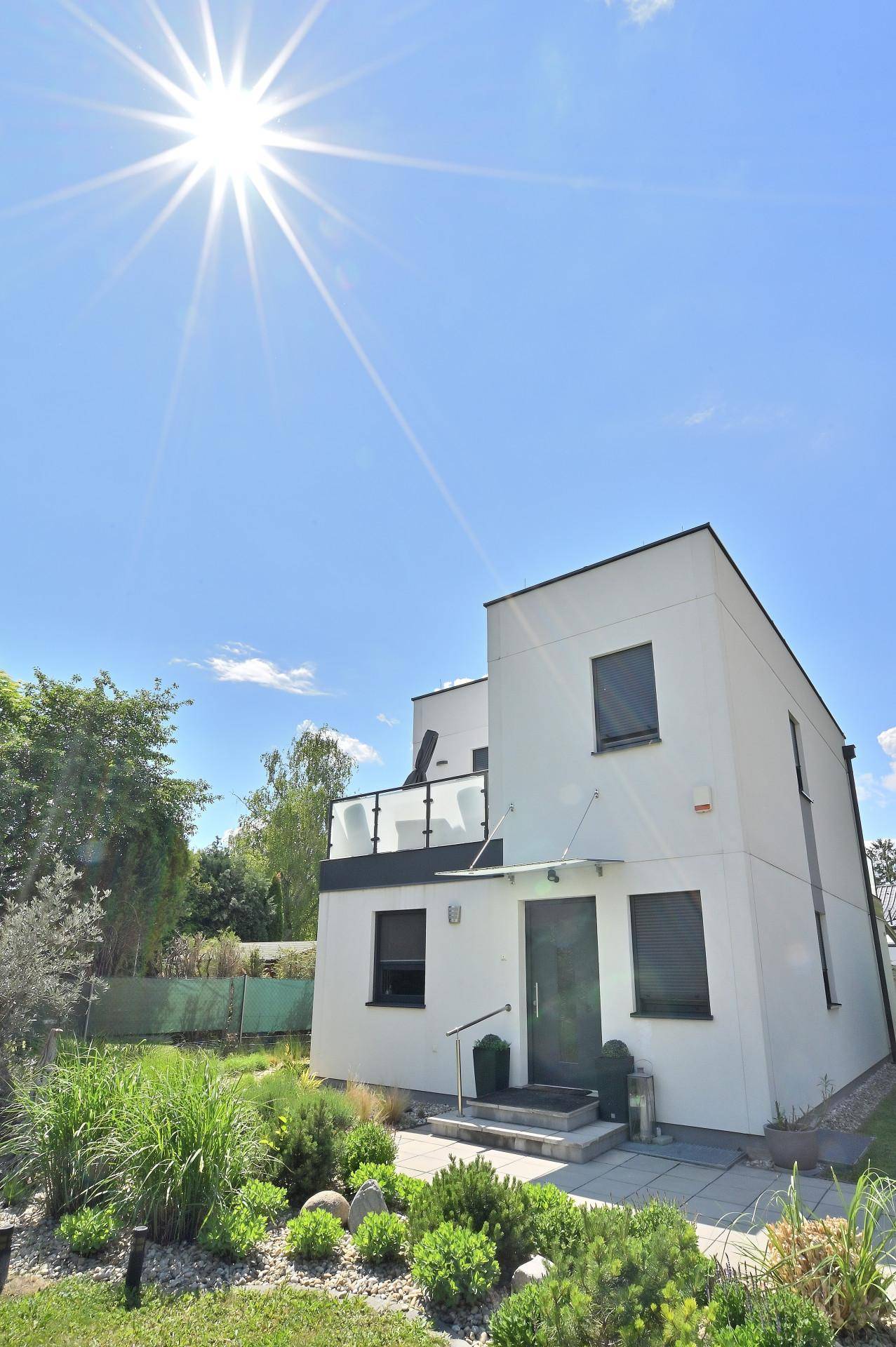 Strahlender Sonnenschein über der modernen Hausfassade mit Balkon und gepflegtem Vorgarten.