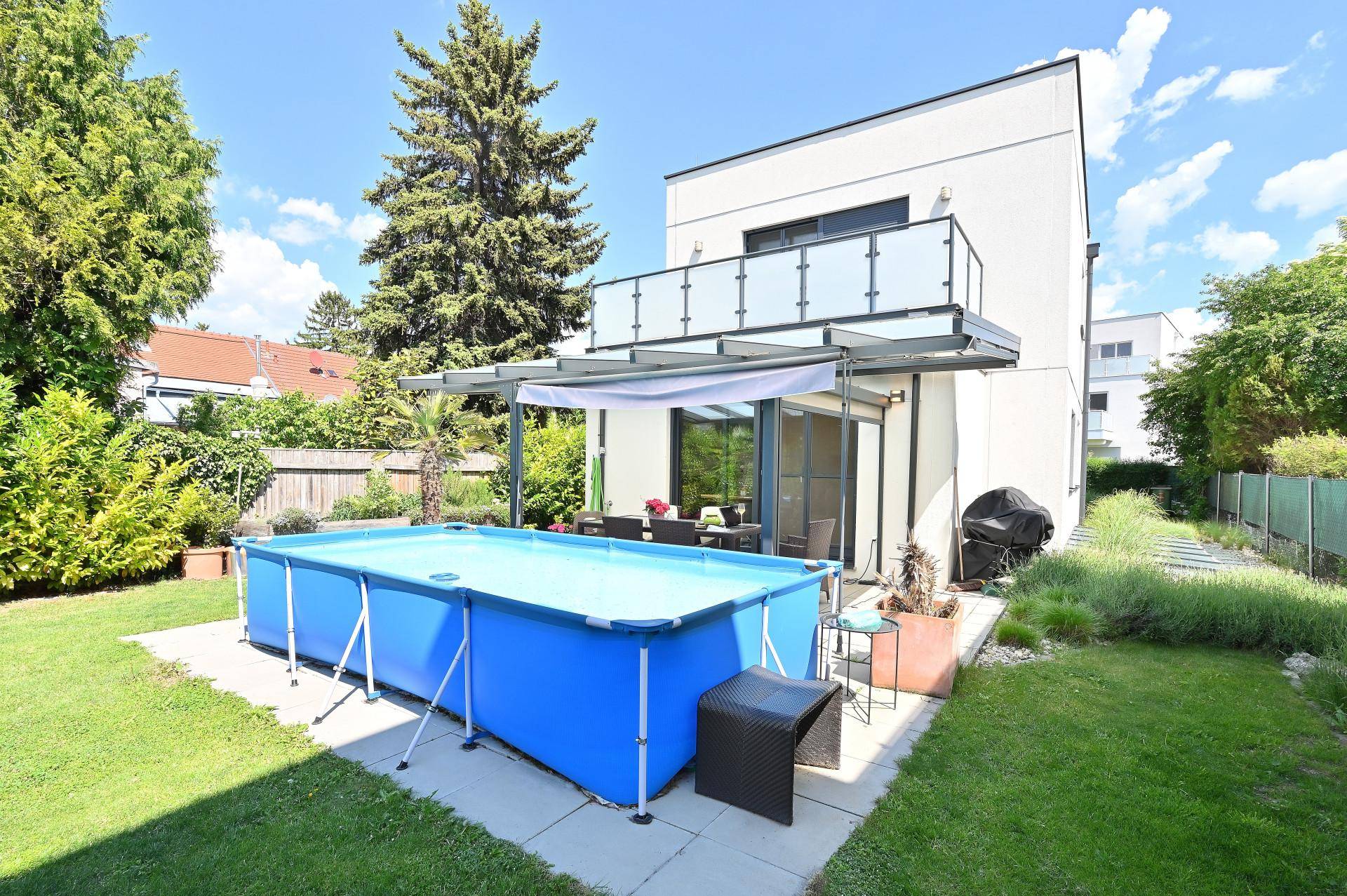 Hinterhof mit großem Aufstellpool, überdachter Terrasse und moderner Hausfassade.