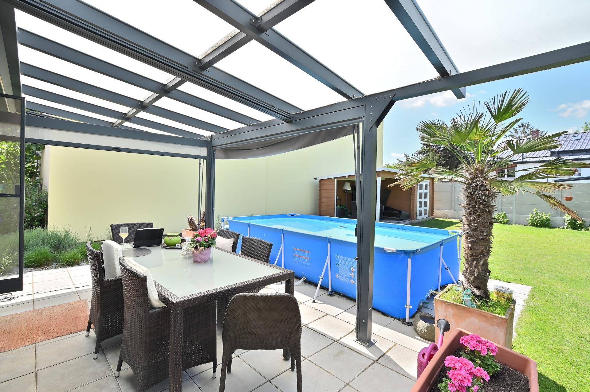 Überdachte Terrasse mit Esstisch und Blick auf den Aufstellpool im sonnigen Garten.