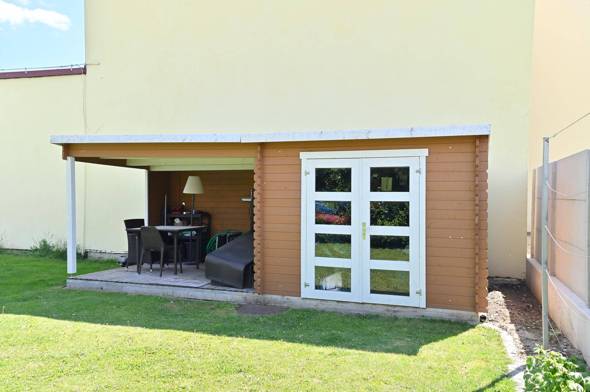 Gemütliches Gartenhaus mit überdachtem Sitzbereich und Blick auf den Rasen.