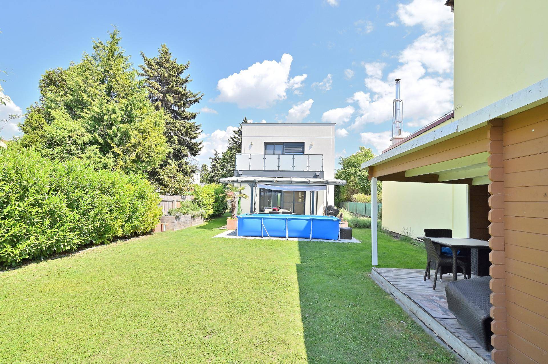 Weitläufiger Garten mit Rasenfläche, Aufstellpool und moderner Hausfassade im Hintergrund.