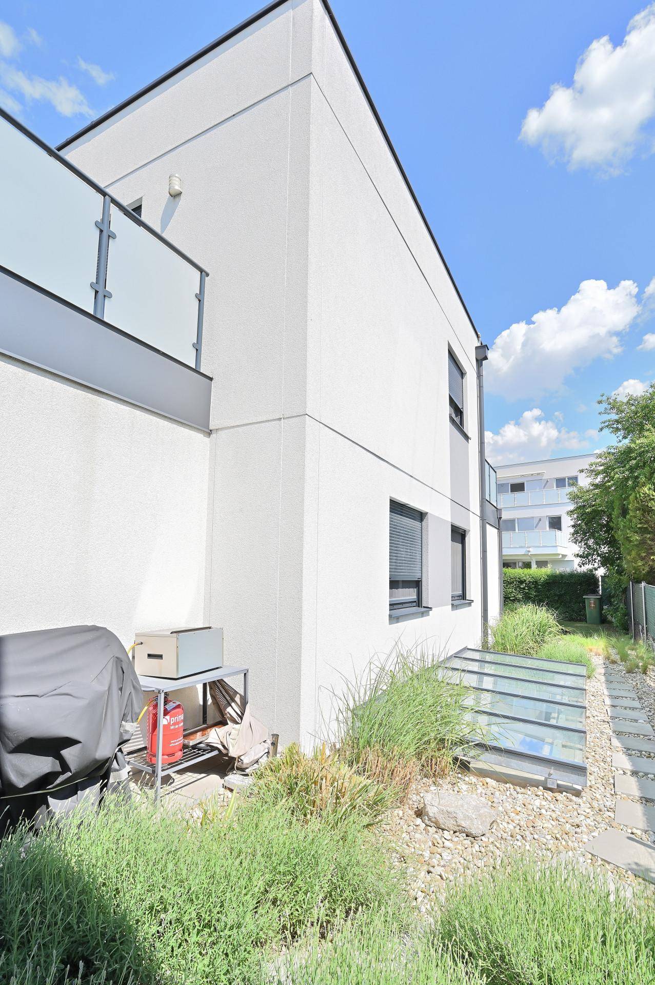 Seitenansicht des modernen Hauses mit Rollläden und Zugang zum Kellerbereich.