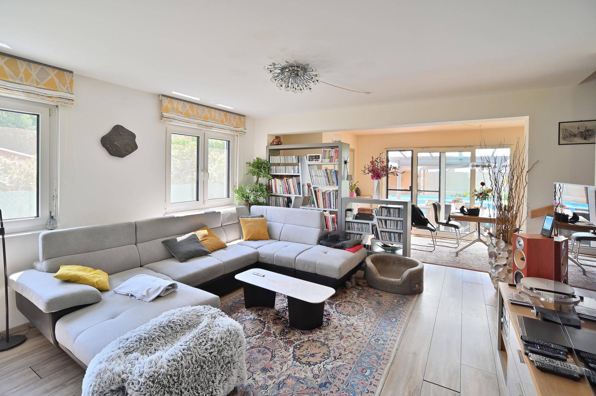 Helles Wohnzimmer mit großem Ecksofa, Holzboden und Blick auf den Essbereich und Garten.