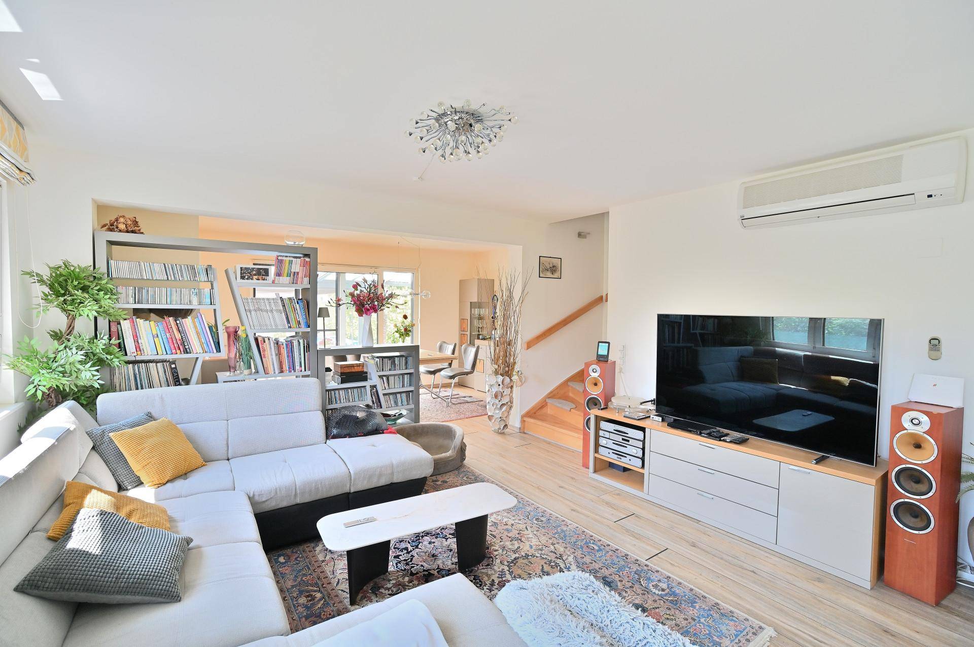 Geräumiges Wohnzimmer mit modernem Sofa, Fernseher und offener Verbindung zum Essbereich.