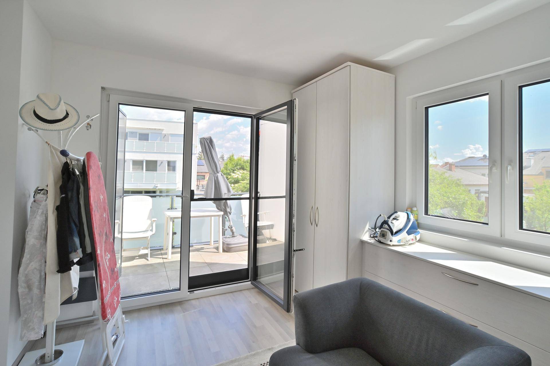 Helles Zimmer mit Schrank, kleiner Couch und Zugang zu einem weiteren Balkon.