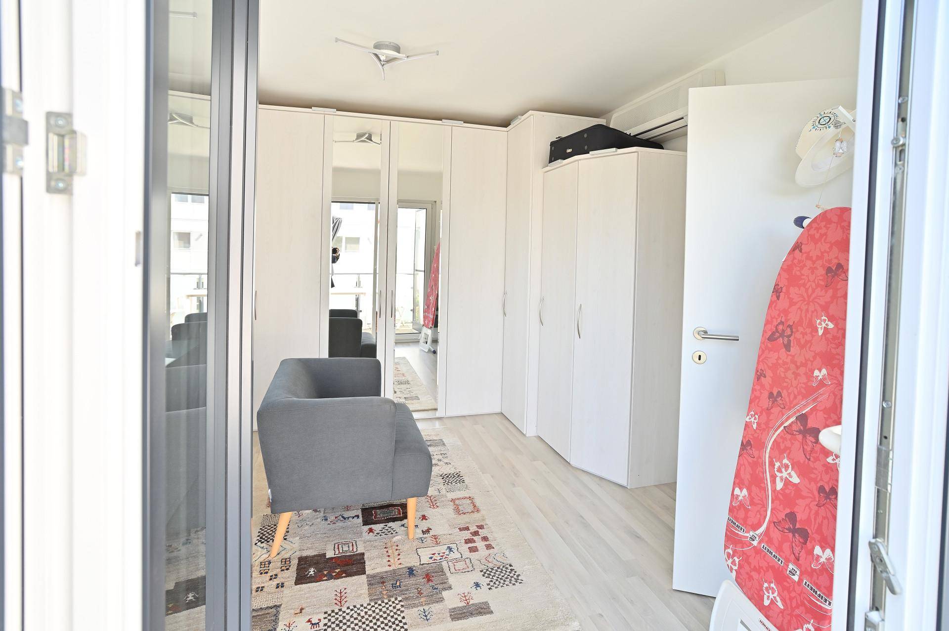 Freundliches Zimmer mit Einbauschränken, kleiner Sitzecke und Zugang zum Außenbereich.
