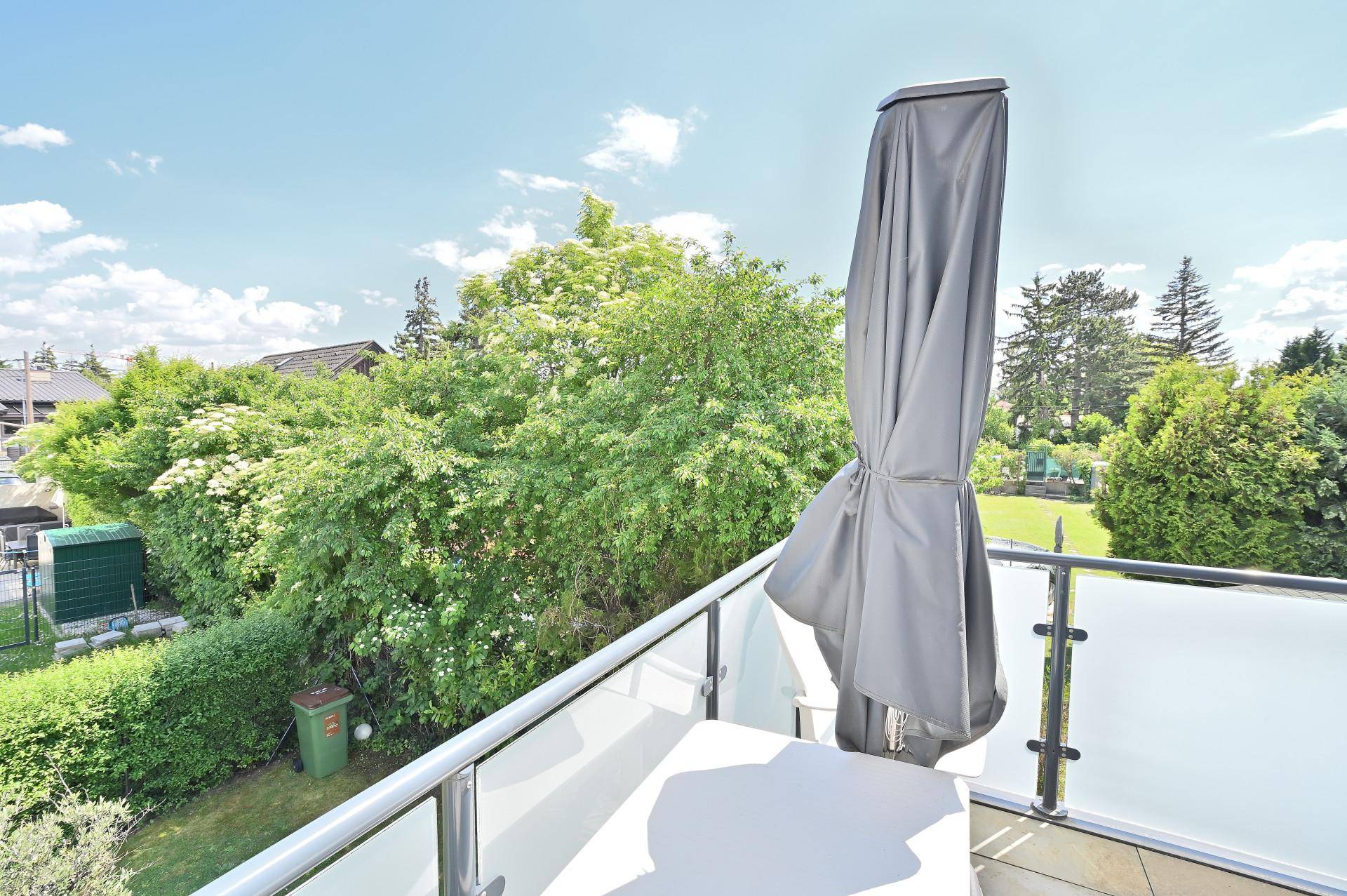 Sonniger Balkon mit Sonnenschirm und weitem Blick über grüne Gärten und Dächer.