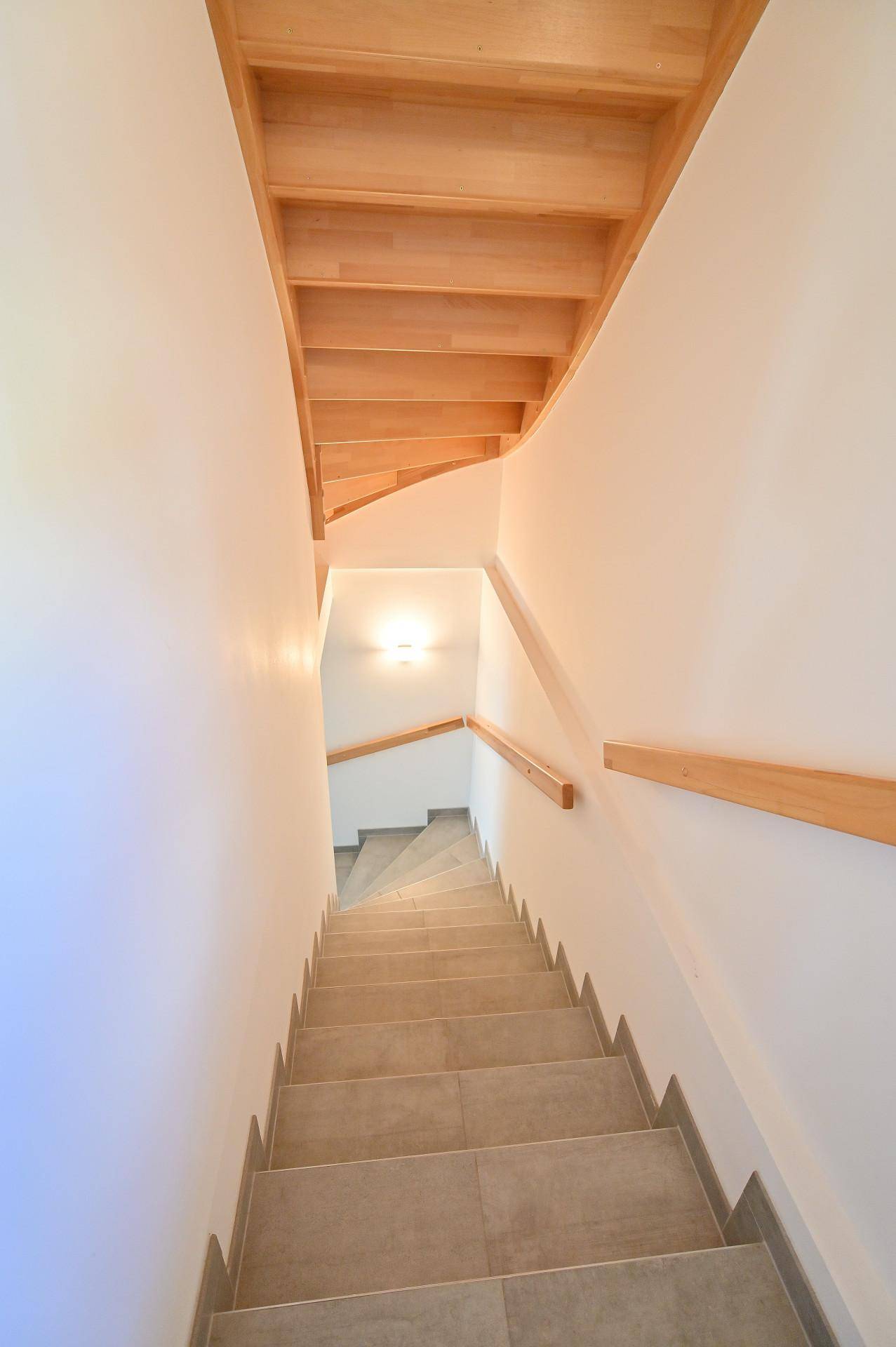 Helles Treppenhaus mit Holzstufen und passenden Holzhandläufen, führt in den unteren Bereich des Hauses.