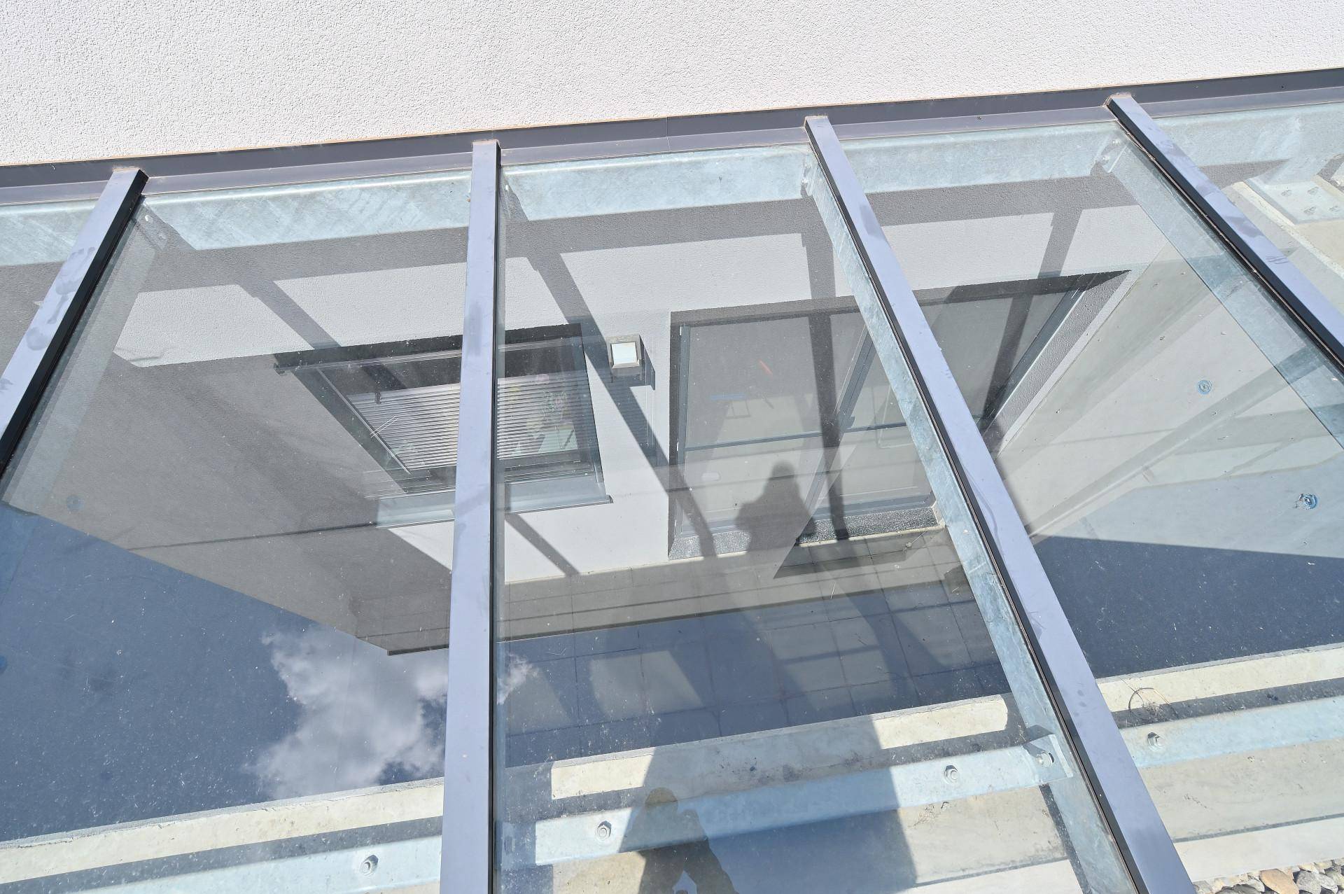 Blick durch eine moderne Glasüberdachung, die den Himmel und die Gebäudefassade mit Fenstern widerspiegelt.