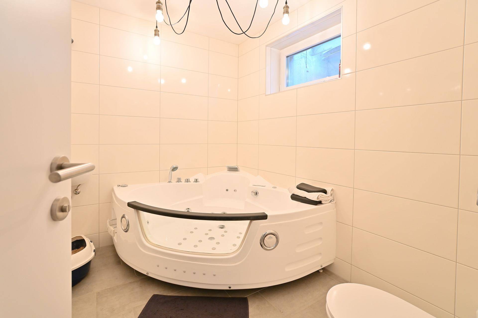 Geräumiges Badezimmer mit großer Eck-Whirlpool-Badewanne und hellen Fliesen an Wänden und Boden.
