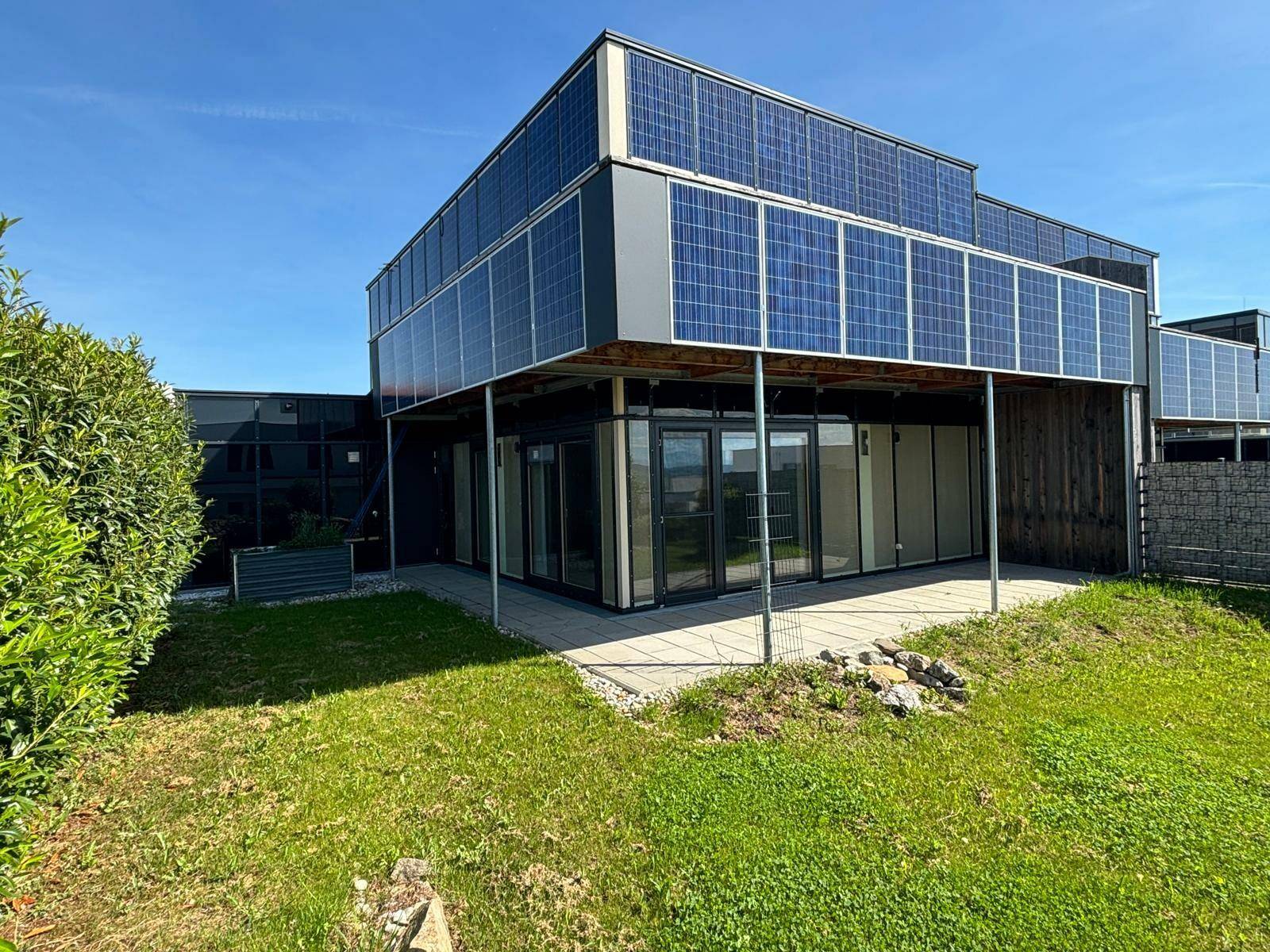 Rückansicht des Gebäudes mit Photovoltaik-Modulen und einem kleinen Gartenbereich.