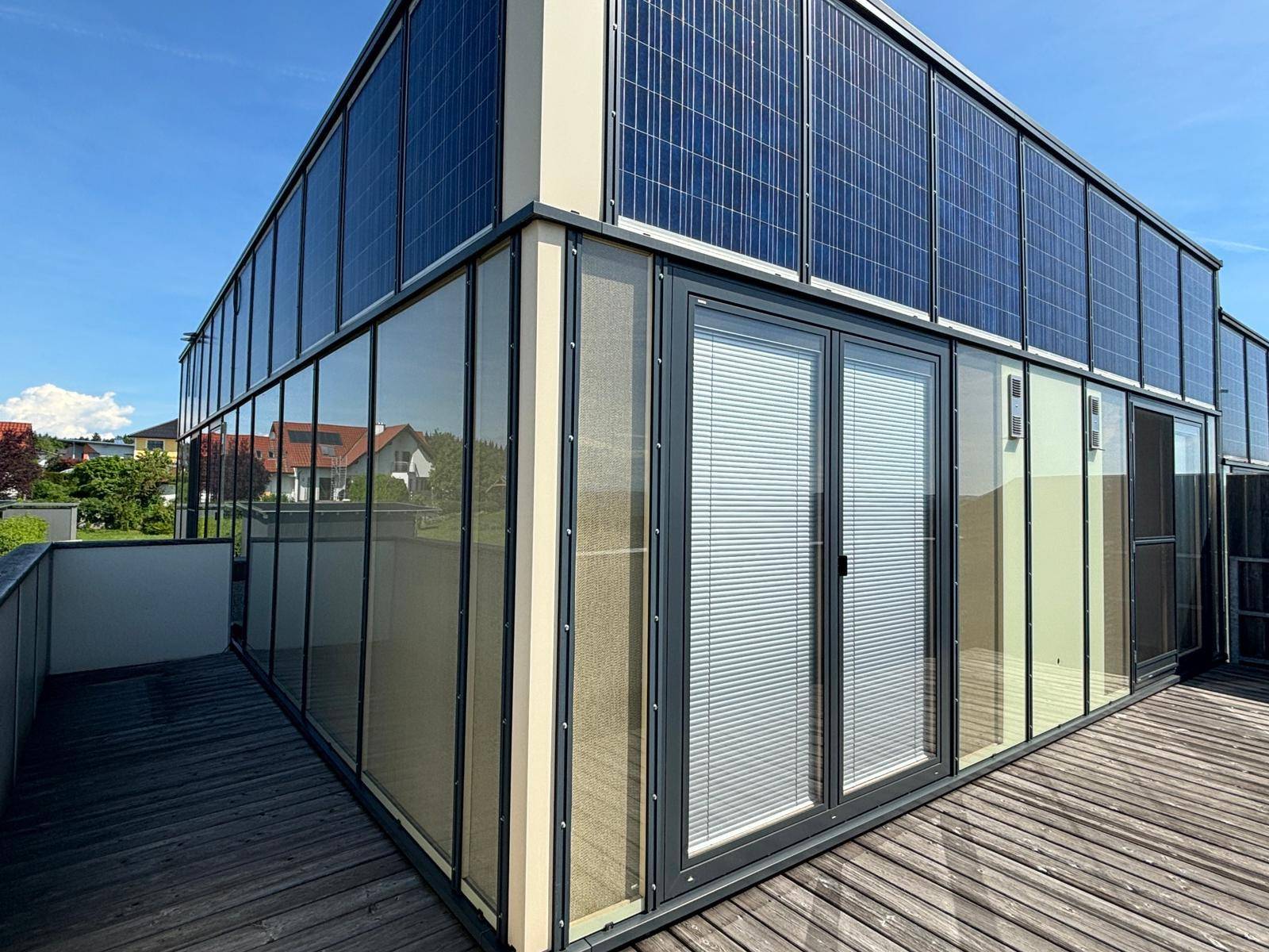 Dachterrasse mit Holzboden und integrierten Photovoltaik-Modulen an der Fassade des Gebäudes.