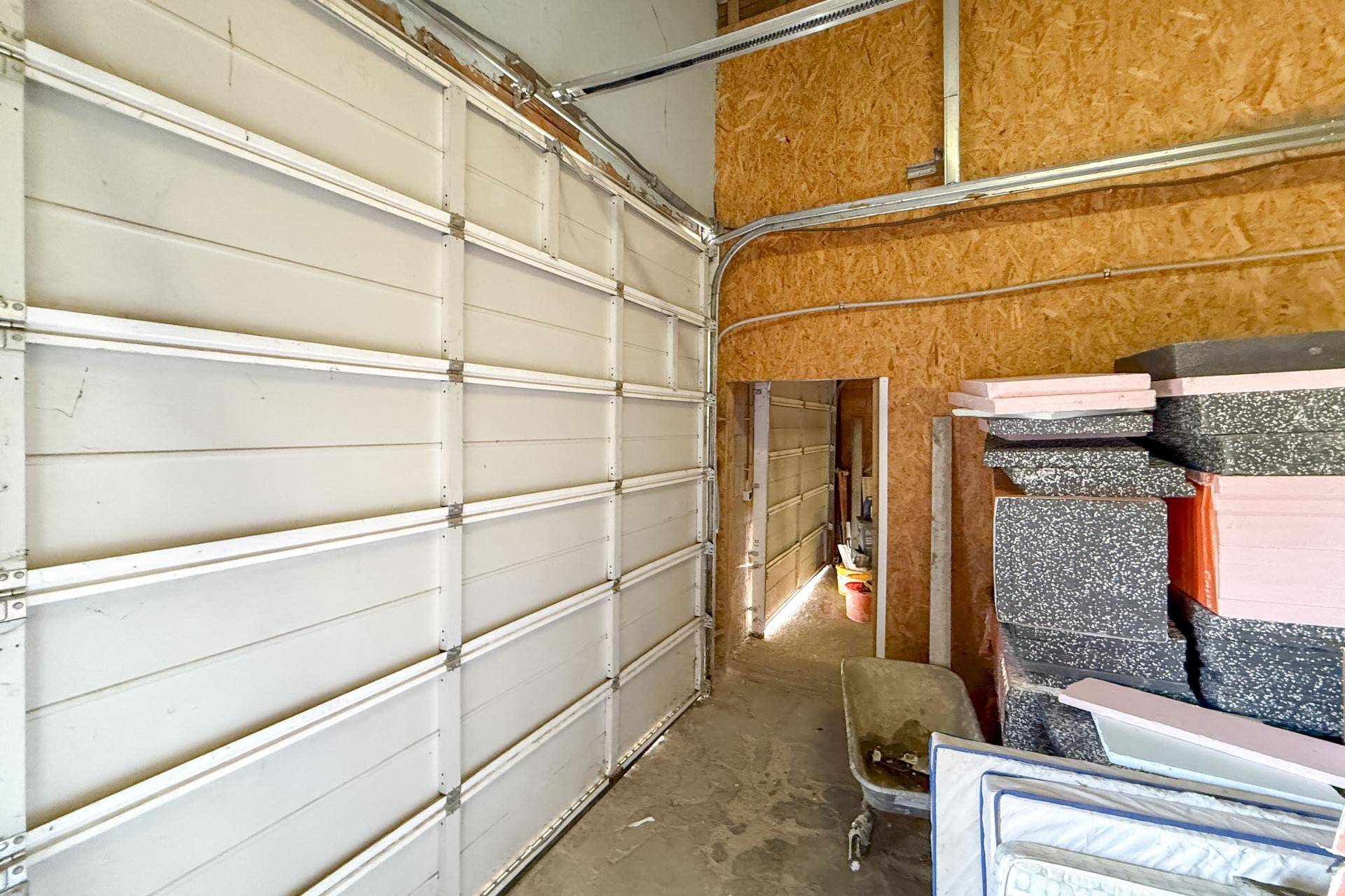 Innenansicht einer Garage mit einem Sektionaltor und gestapelten Dämmmaterialien an der Seite.
