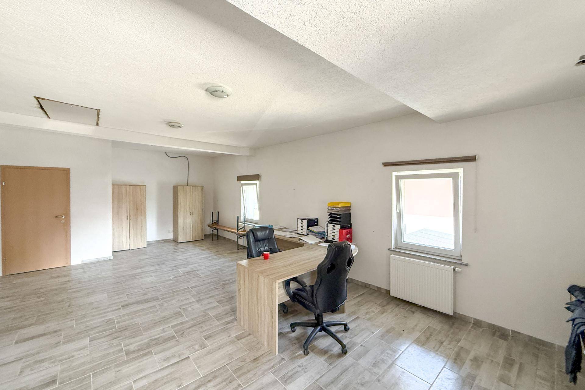 Geräumiges Büro mit hellen Wänden, gefliestem Boden und einem Schreibtisch mit Bürostuhl.