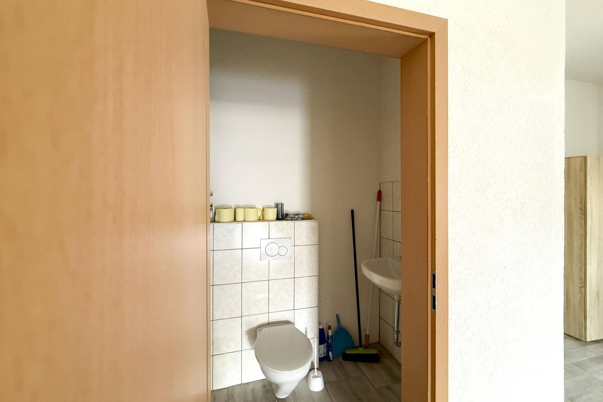 Einfache Gästetoilette mit WC, kleinem Waschbecken und hellen Fliesen an den Wänden.