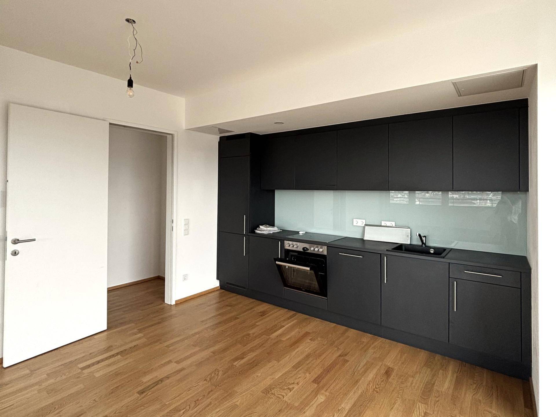 Moderne, dunkle Küche mit integrierten Geräten und Holzboden in einem leeren Raum.