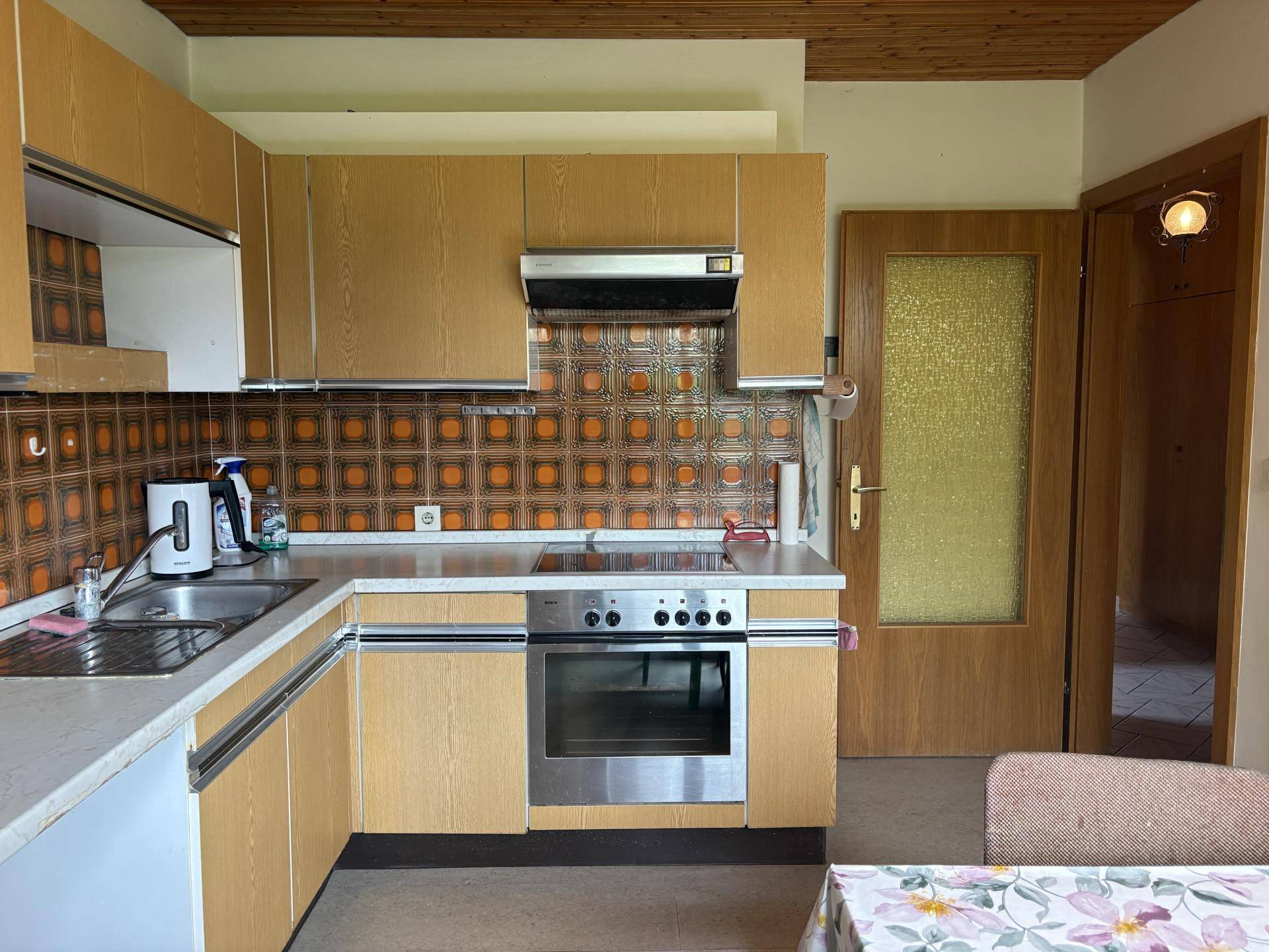 Ältere Küche mit Holzschränken, gemusterten Fliesen und integriertem Backofen, die einen funktionalen Raum bietet.