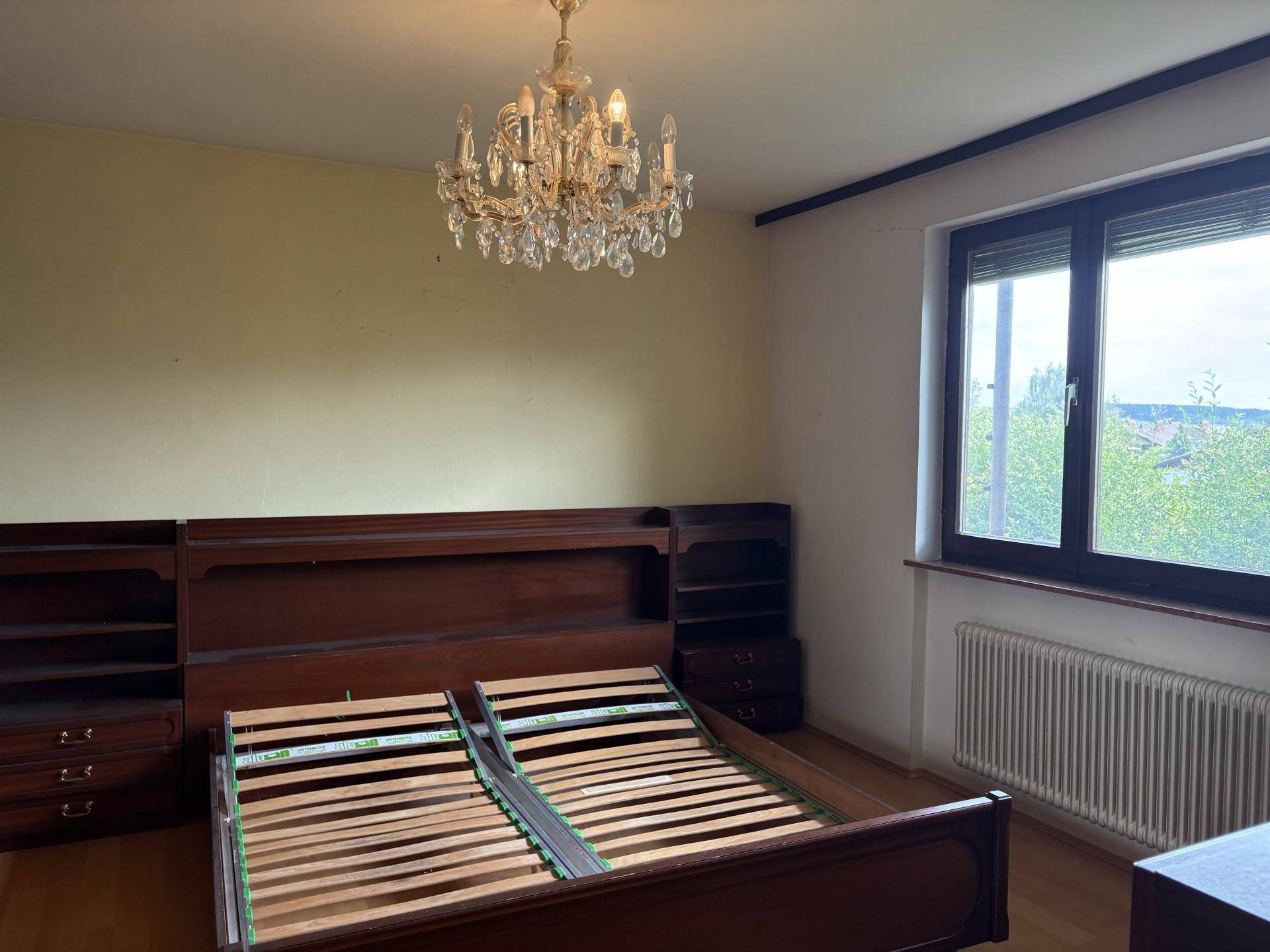 Schlafzimmer mit Holzboden, großem Fenster und einem Kronleuchter, der dem Raum eine elegante Note verleiht.