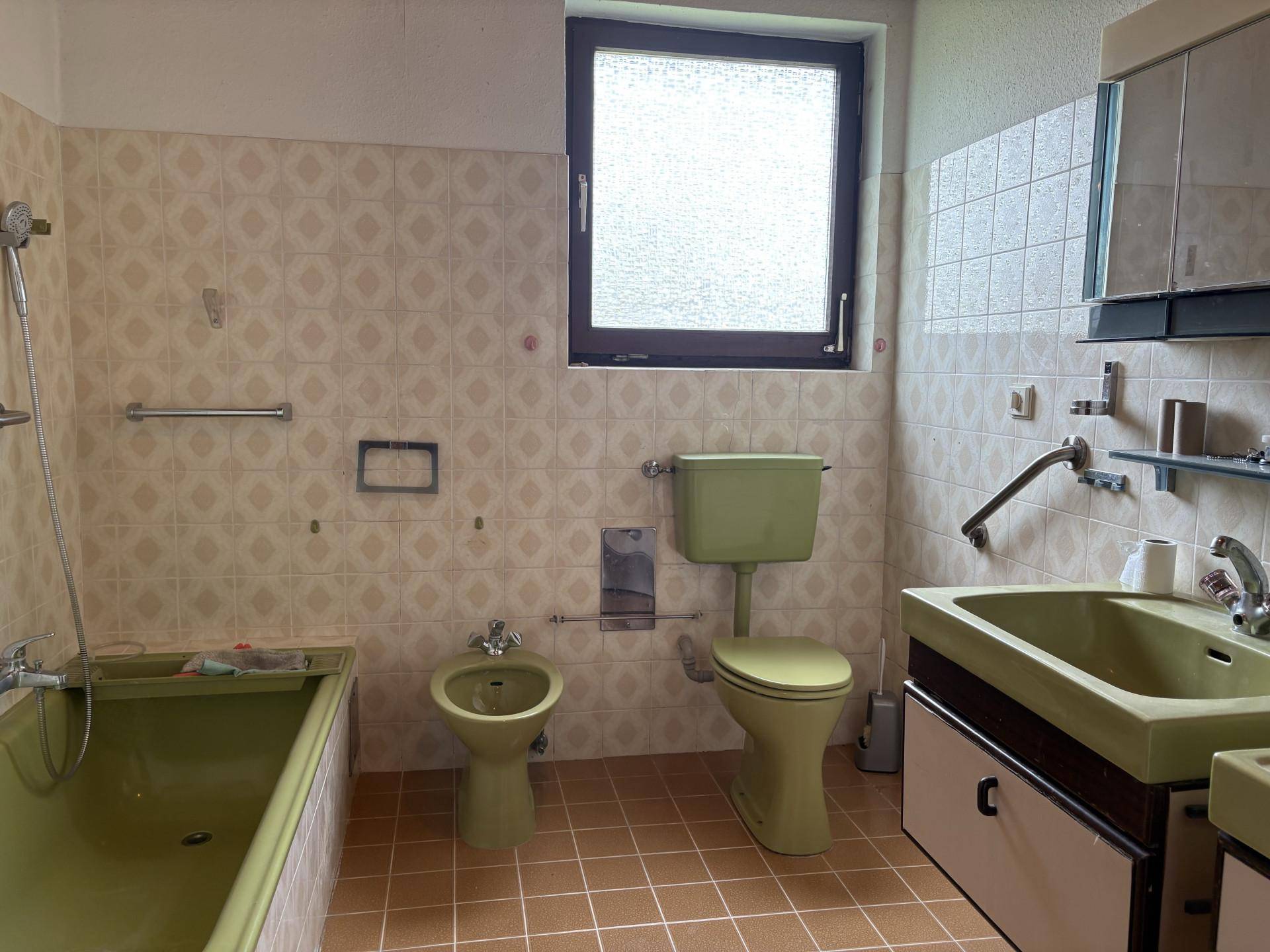 Badezimmer im Stil der 80er Jahre mit grünen Sanitärobjekten, Badewanne, Bidet und gemusterten Wandfliesen.