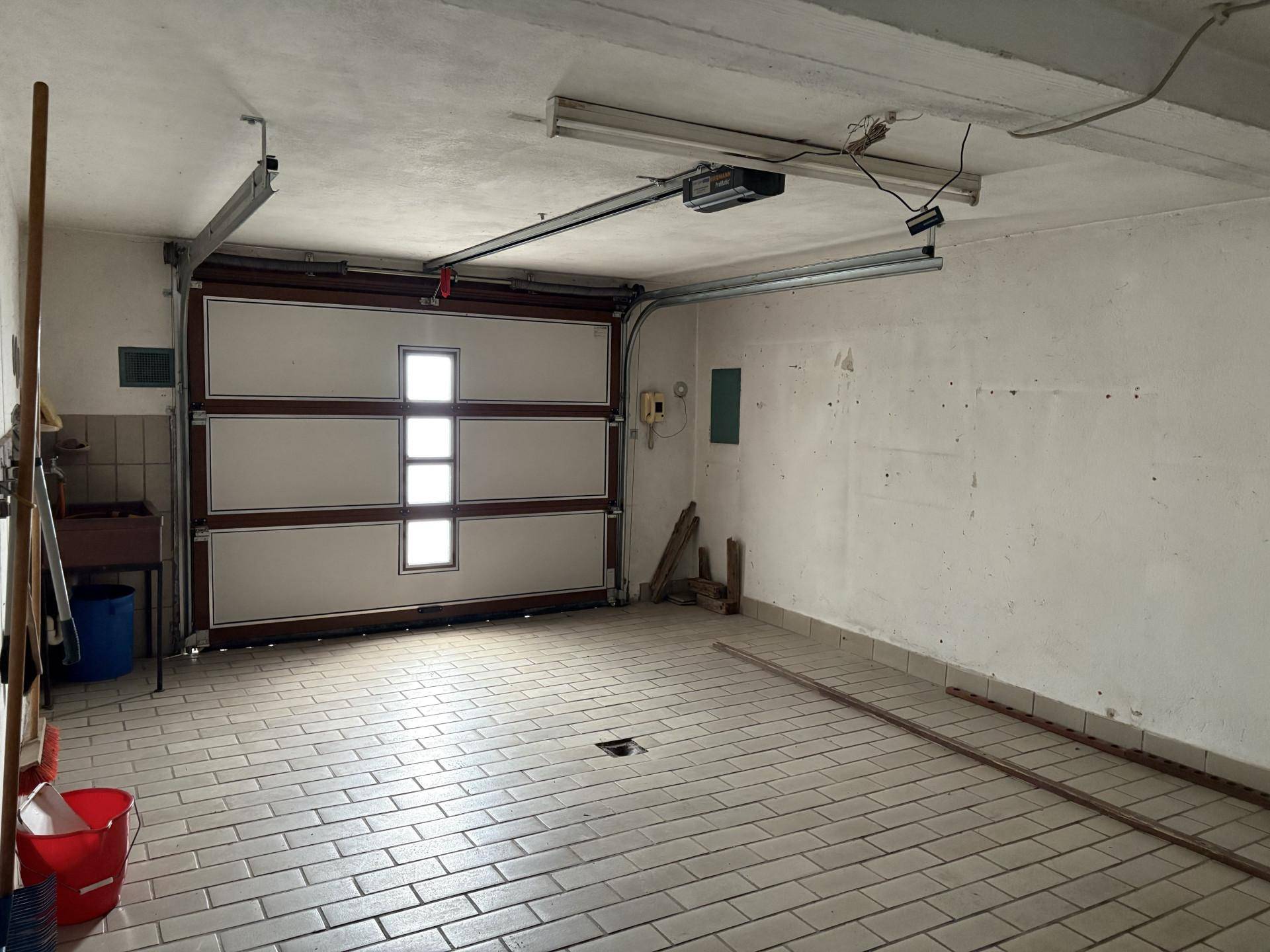 Geräumige Garage mit Fliesenboden und automatischem Garagentor, die Platz für ein Fahrzeug bietet.