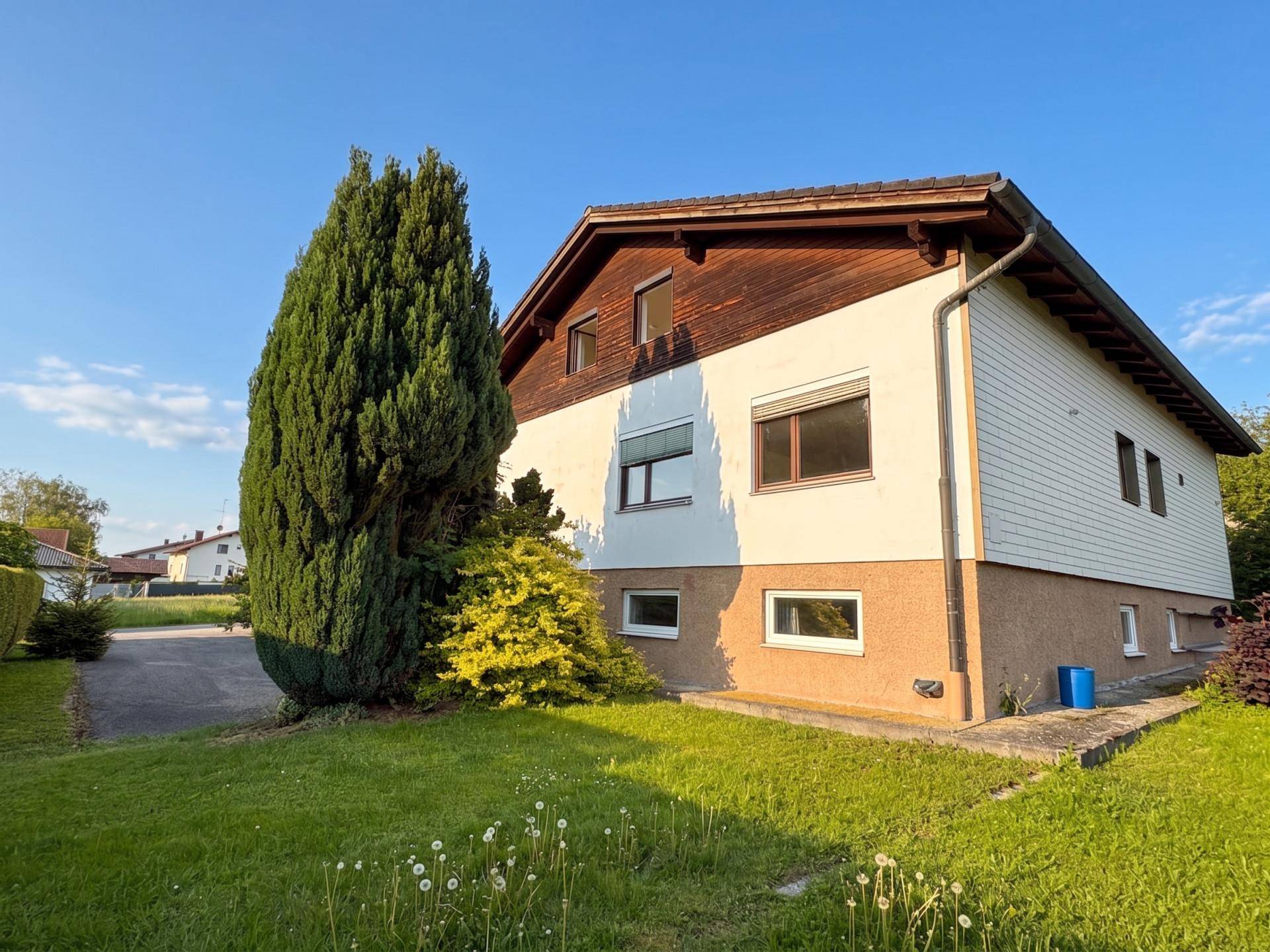 Seitenansicht des Hauses mit weißer Fassade, Holzverkleidung und einem gepflegten Rasen im Vordergrund.