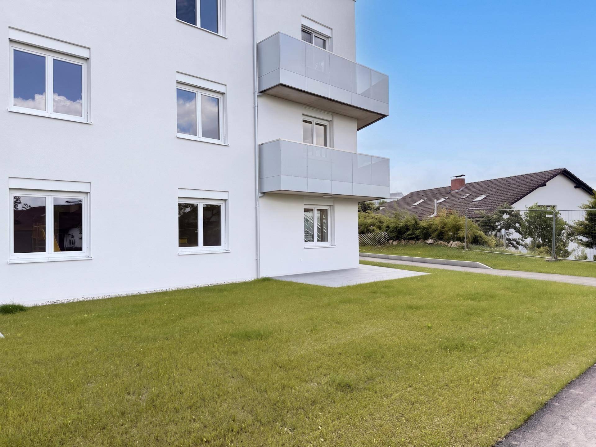 Moderne Gebäudefassade eines Neubaus mit Balkonen und gepflegter Rasenfläche im Außenbereich.