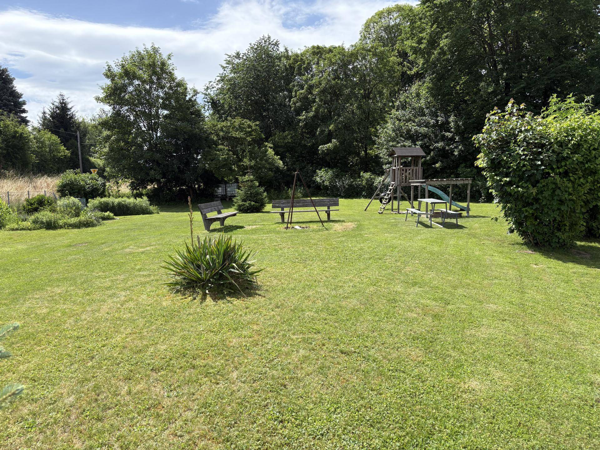 Großer Gemeinschaftsgarten mit Spielplatz, Sitzbänken und altem Baumbestand.
