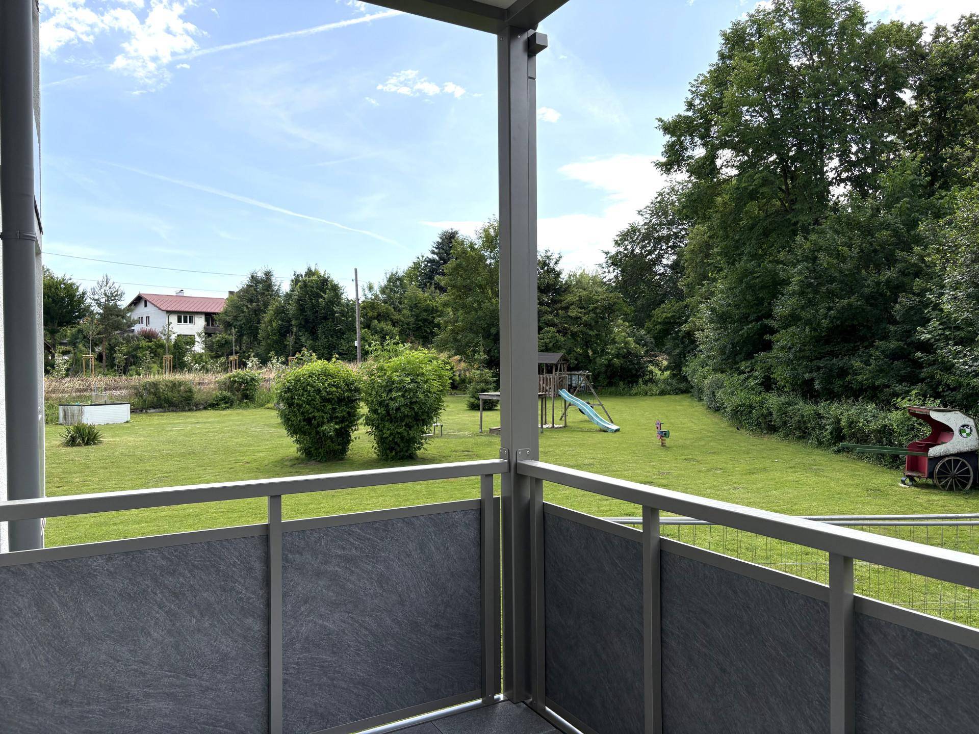 Balkon mit Blick auf den grünen Gemeinschaftsgarten und den Kinderspielplatz.
