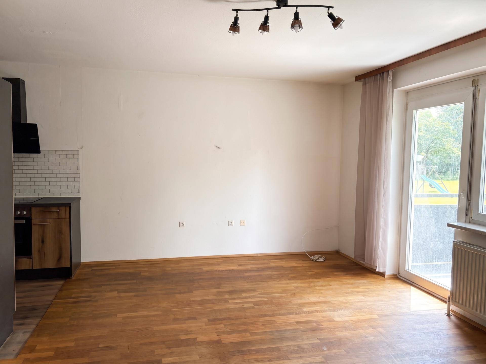 Heller Wohnbereich mit Laminatboden und Zugang zu einem Balkon oder einer Terrasse.