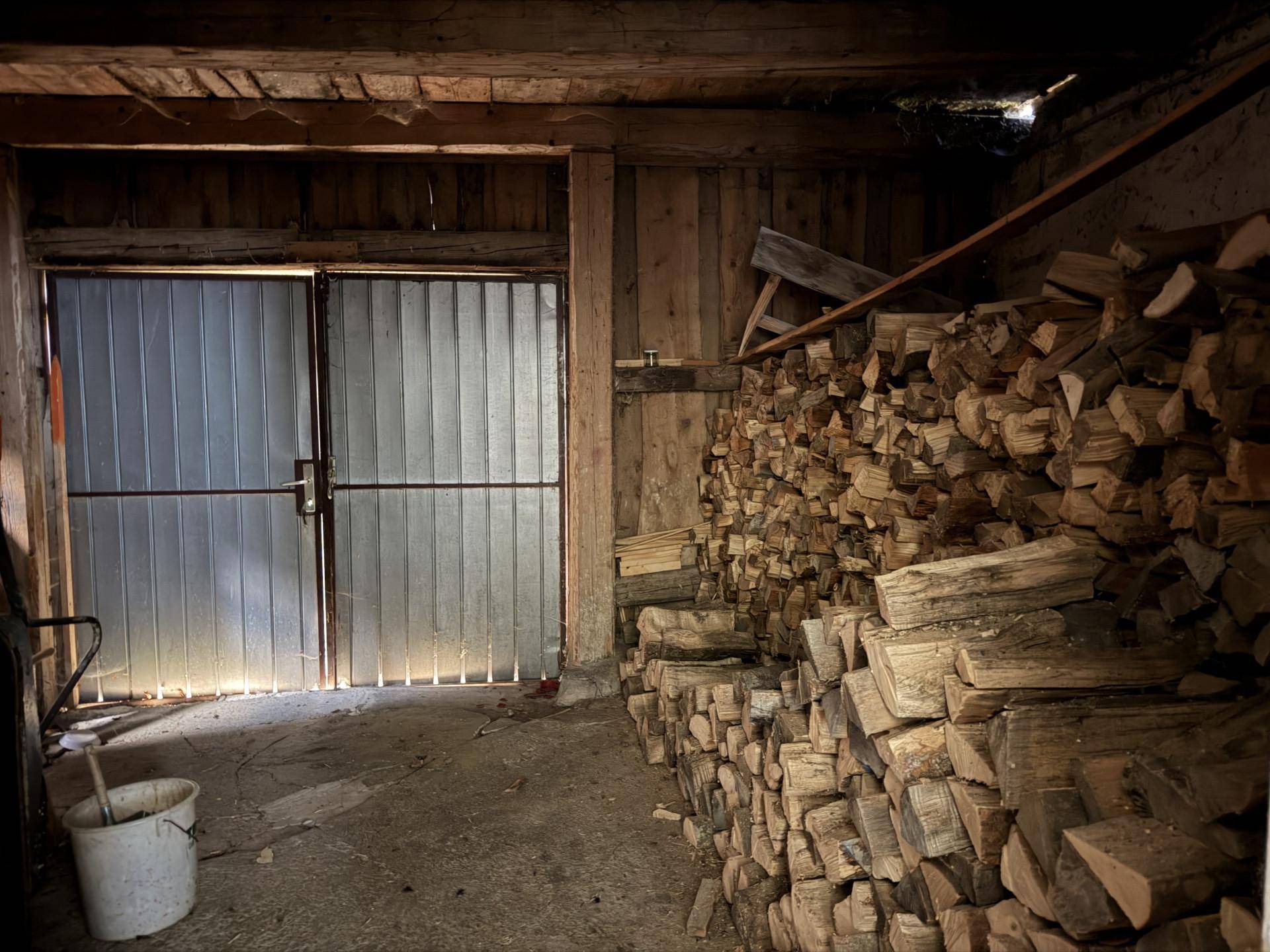 Großer Lagerraum mit Holzbalken, Metalltüren und gestapeltem Brennholz.