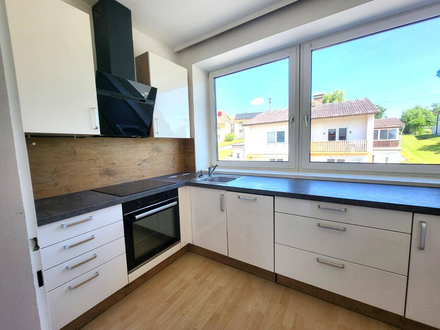 Moderne Küche mit weißen Hochglanzschränken, dunkler Arbeitsplatte und Blick ins Grüne.